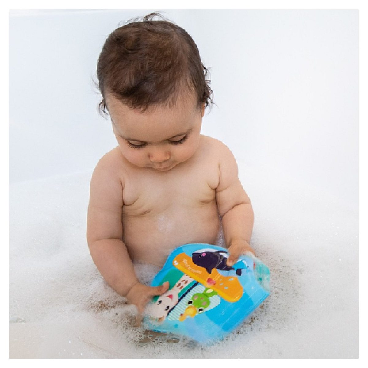 Ein Baby sitzt in einer Badewanne voll Schaum und spielt mit einem bunten Wasserspielzeug.