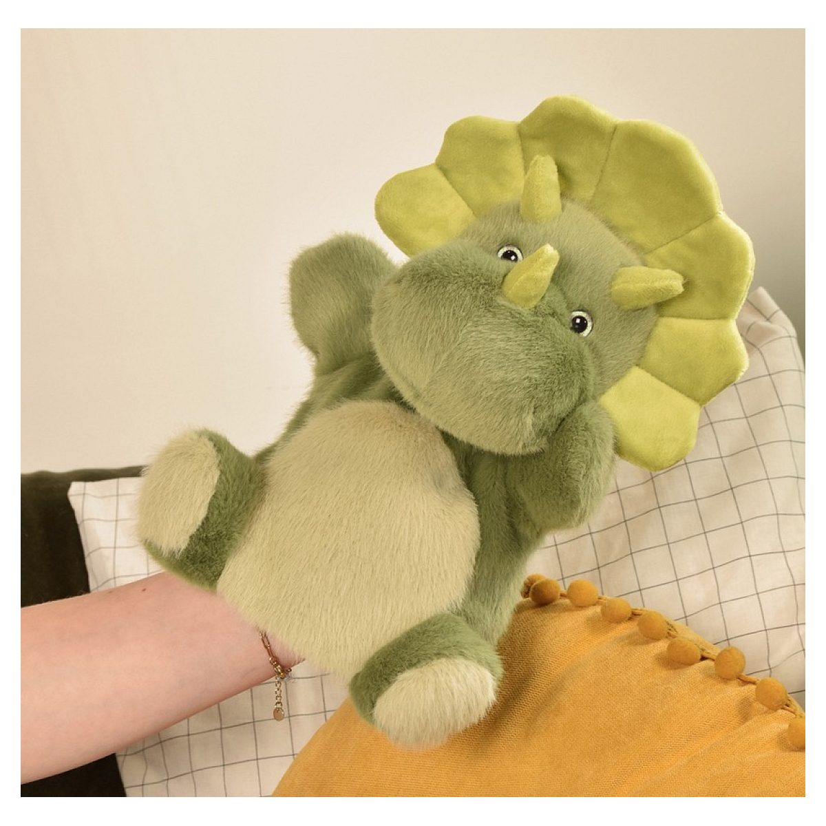 Eine grüne Triceratops-Handpuppe vor Kissen.