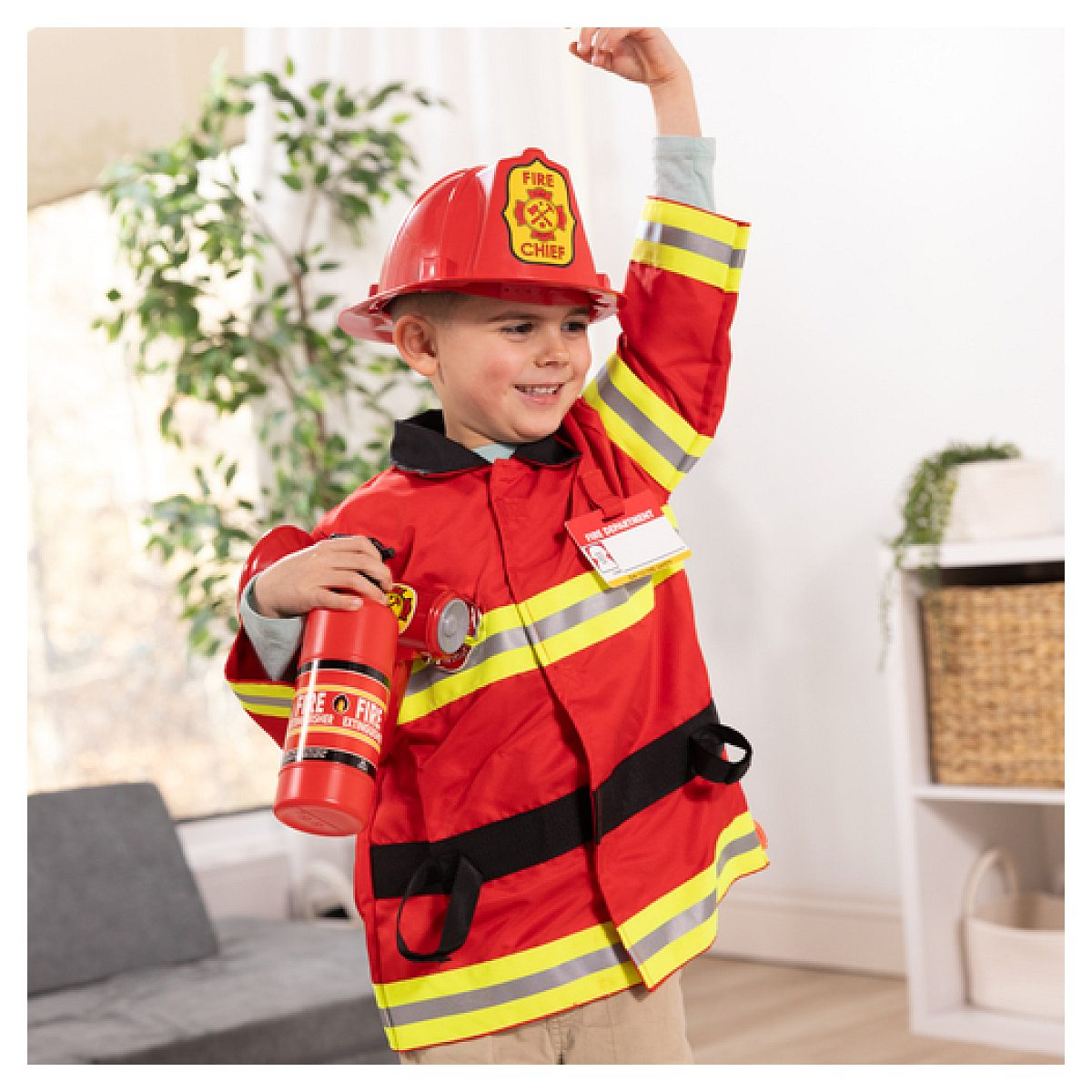 Niño disfrazado de bombero sostiene un extintor de juguete rojo en una habitación luminosa.