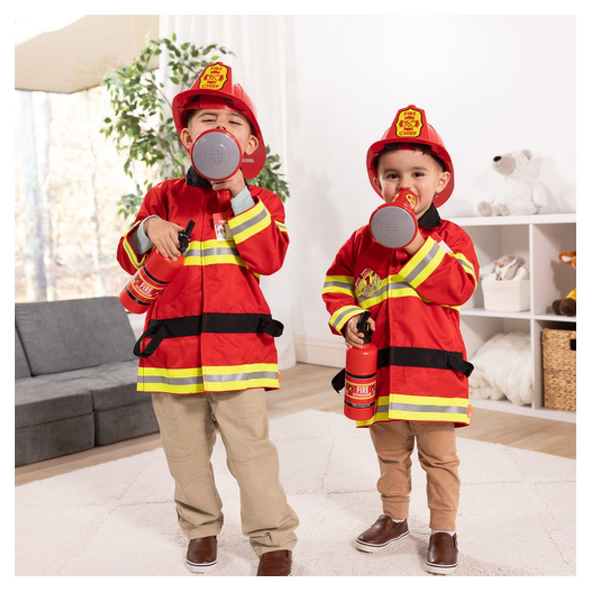 Dos niños pequeños con disfraces de bomberos sostienen megáfonos y extintores de juguete en una habitación luminosa.
