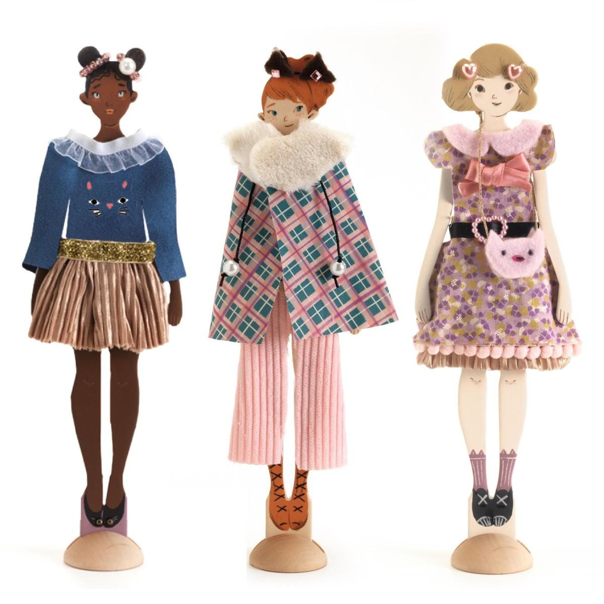Drei Modepuppen aus Holz mit bunten Outfits und Accessoires stehen auf runden Sockeln vor weißem Hintergrund.