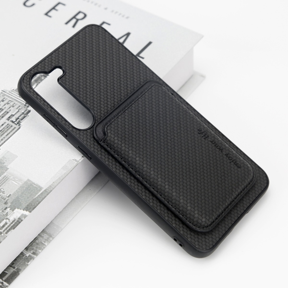 Eine schwarze Smartphone-Hülle aus Kohlefaser mit Brieftasche liegt auf einem Buch.