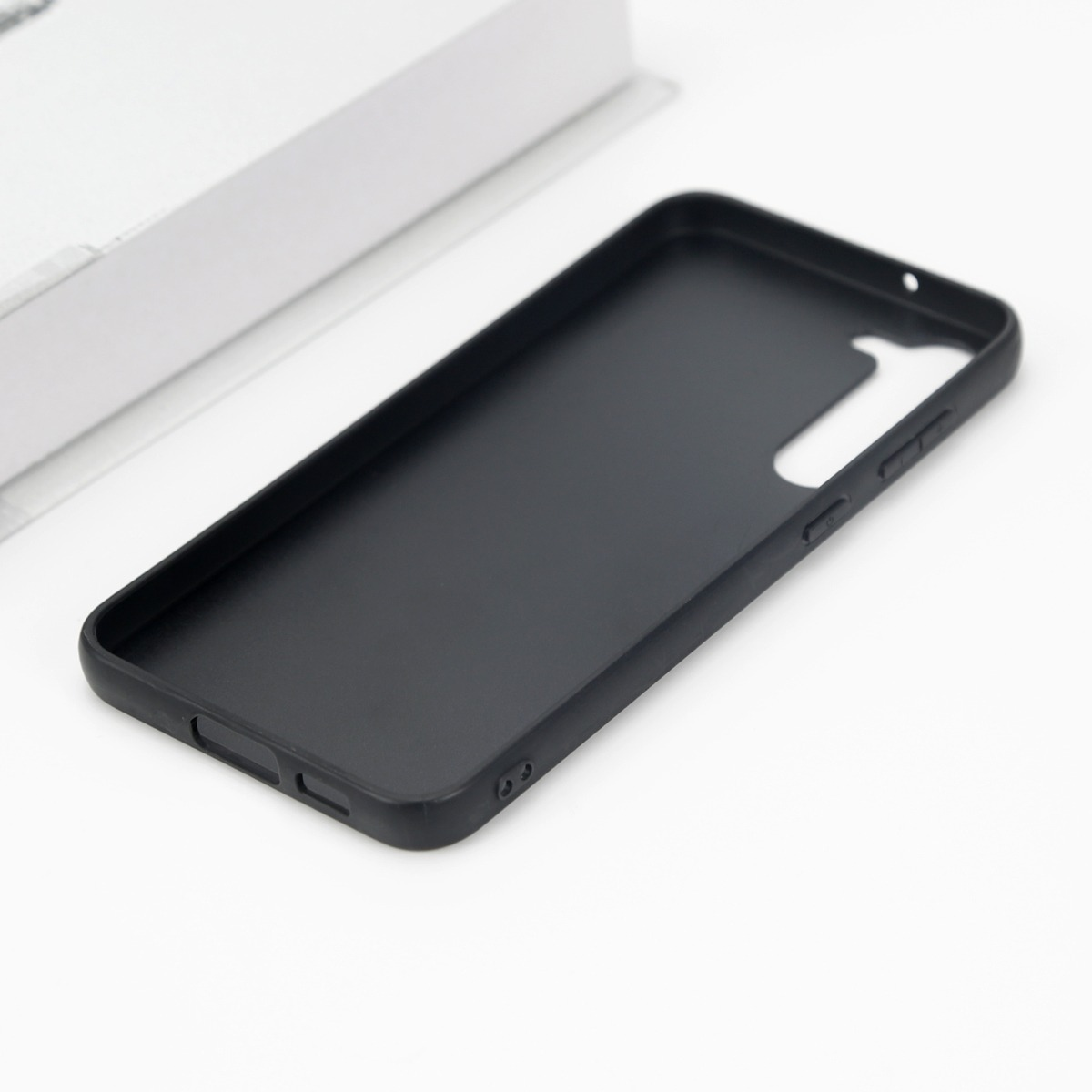Eine schwarze Smartphone-Hülle liegt auf einer weißen Oberfläche neben einer weißen Box.