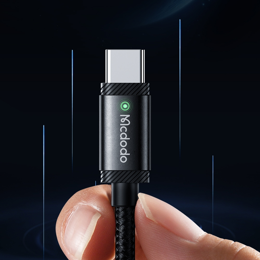 Mano tiene un cavo USB-C nero con corpo in metallo e luce LED verde su sfondo scuro.