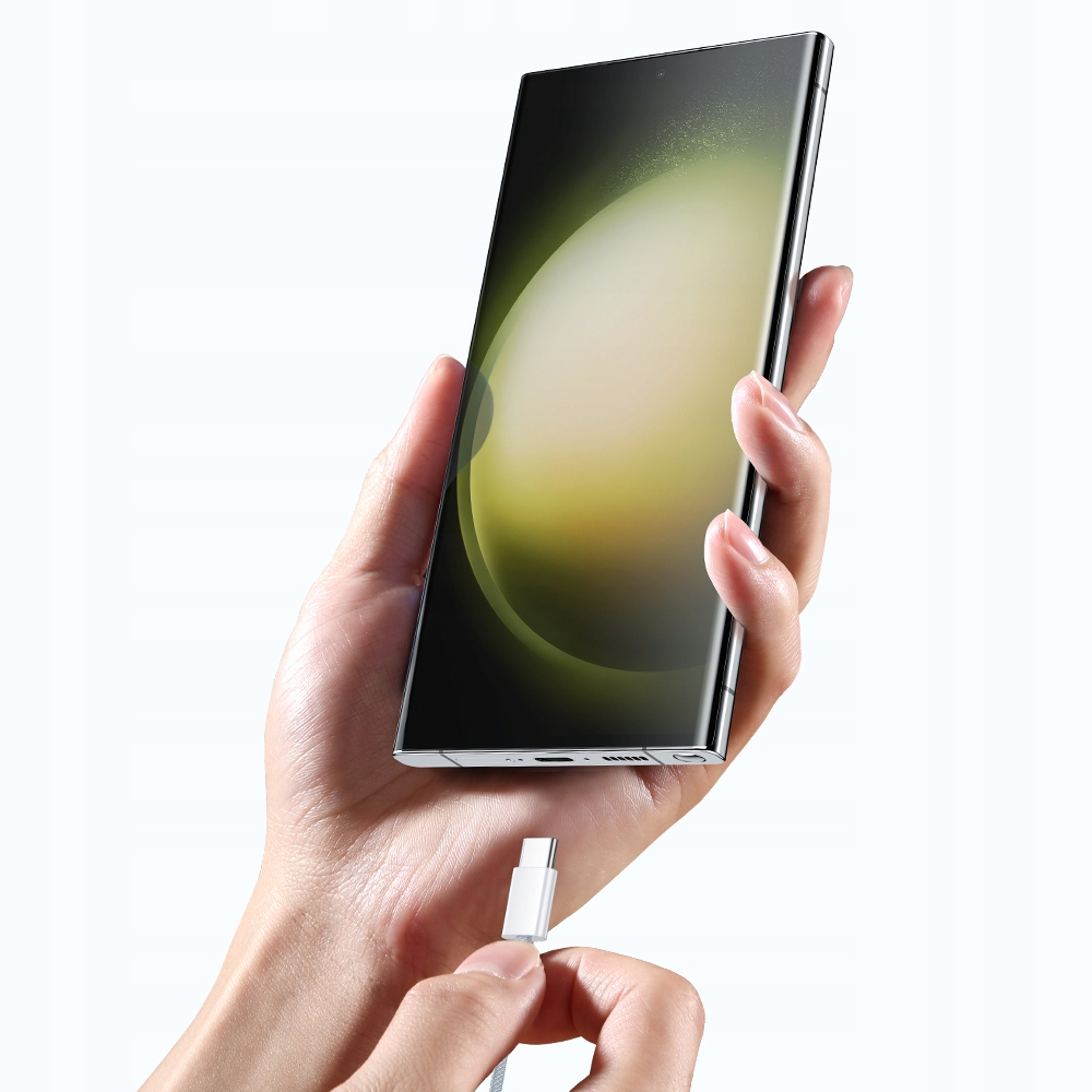 Una mano tiene uno smartphone mentre un'altra inserisce un cavo di ricarica USB-C.