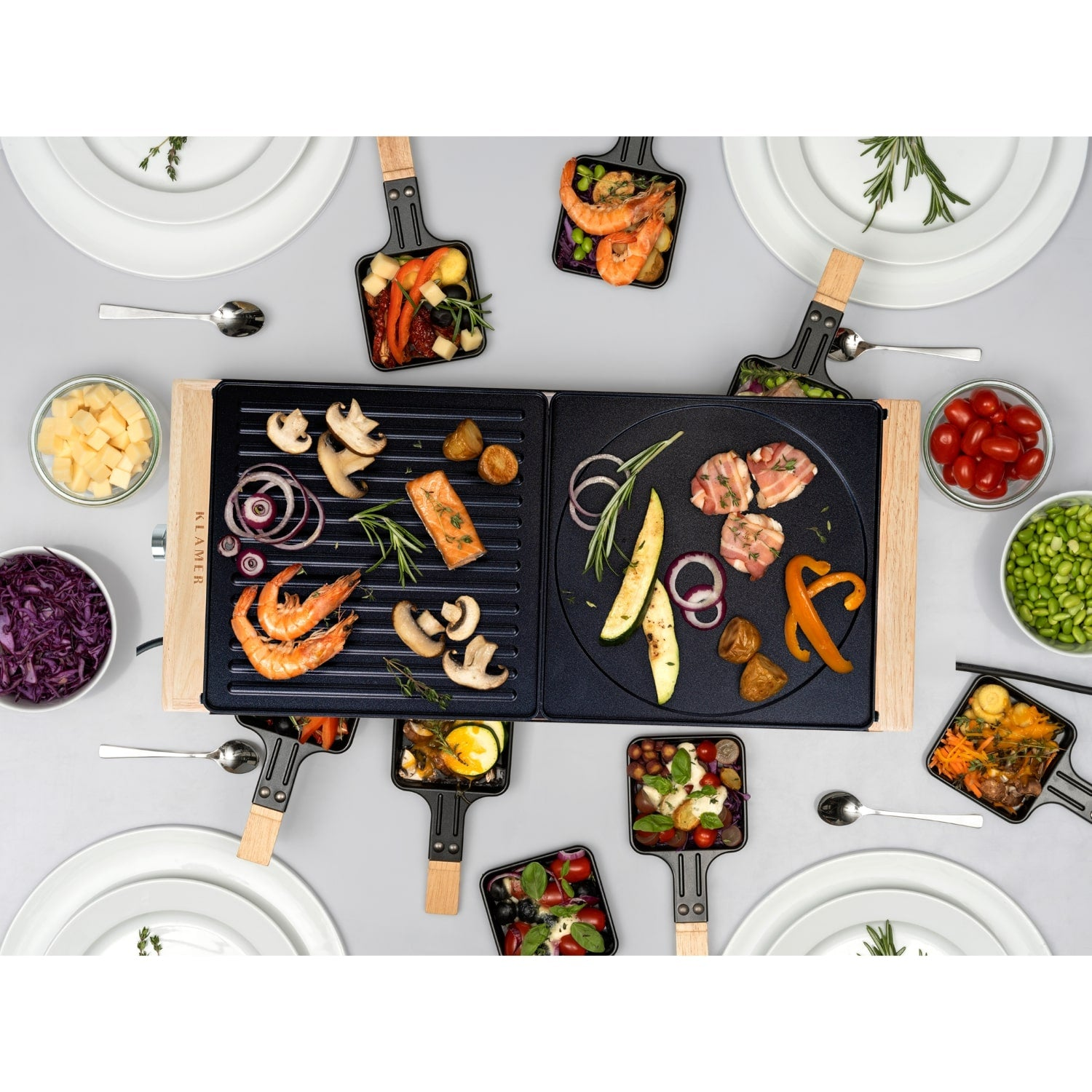 Ein Raclette-Grill mit Garnelen, Pilzen und Fleisch, umgeben von Schüsseln mit Gemüse und leeren Tellern.