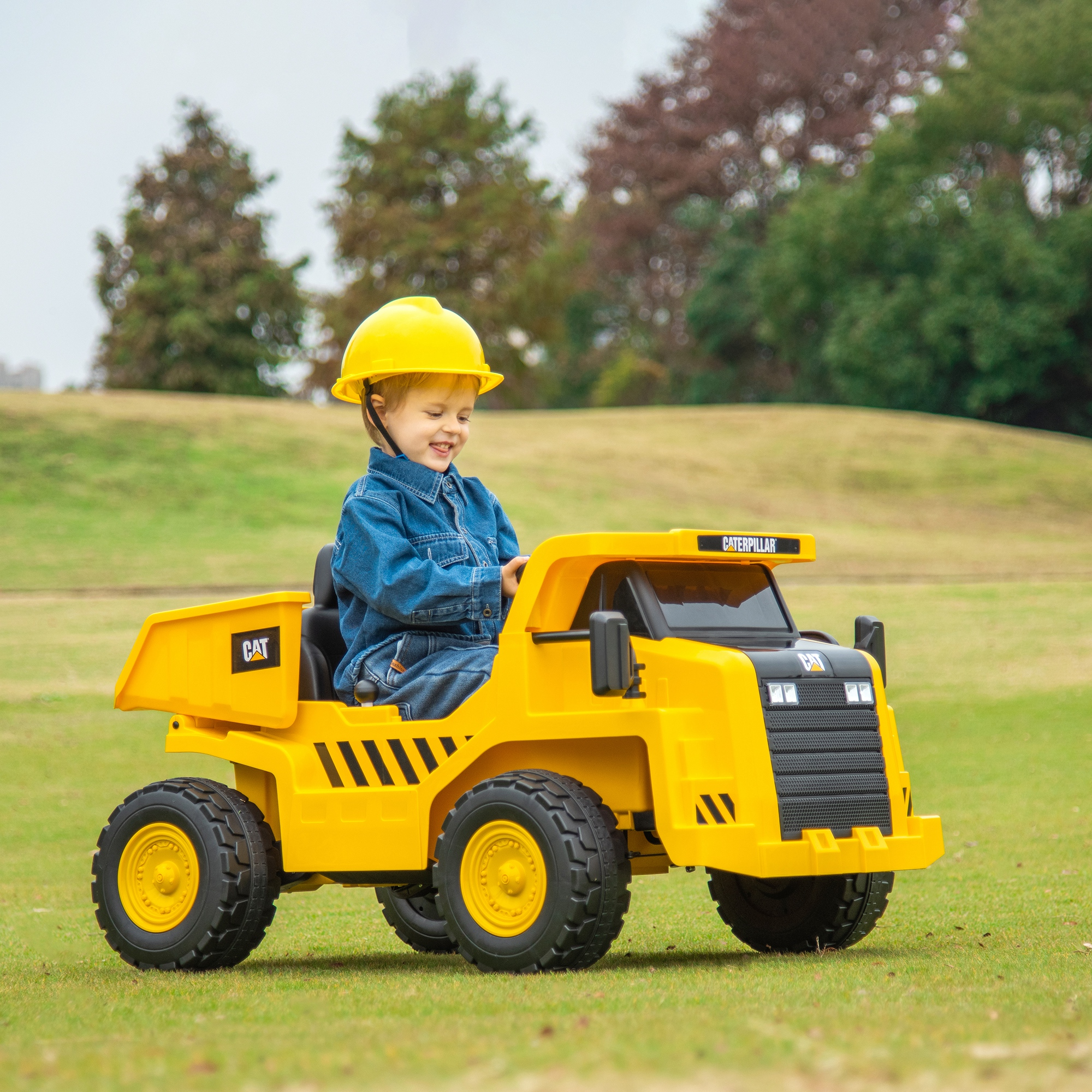 Un bambino sorridente con elmetto giallo guida un camion giocattolo CAT.