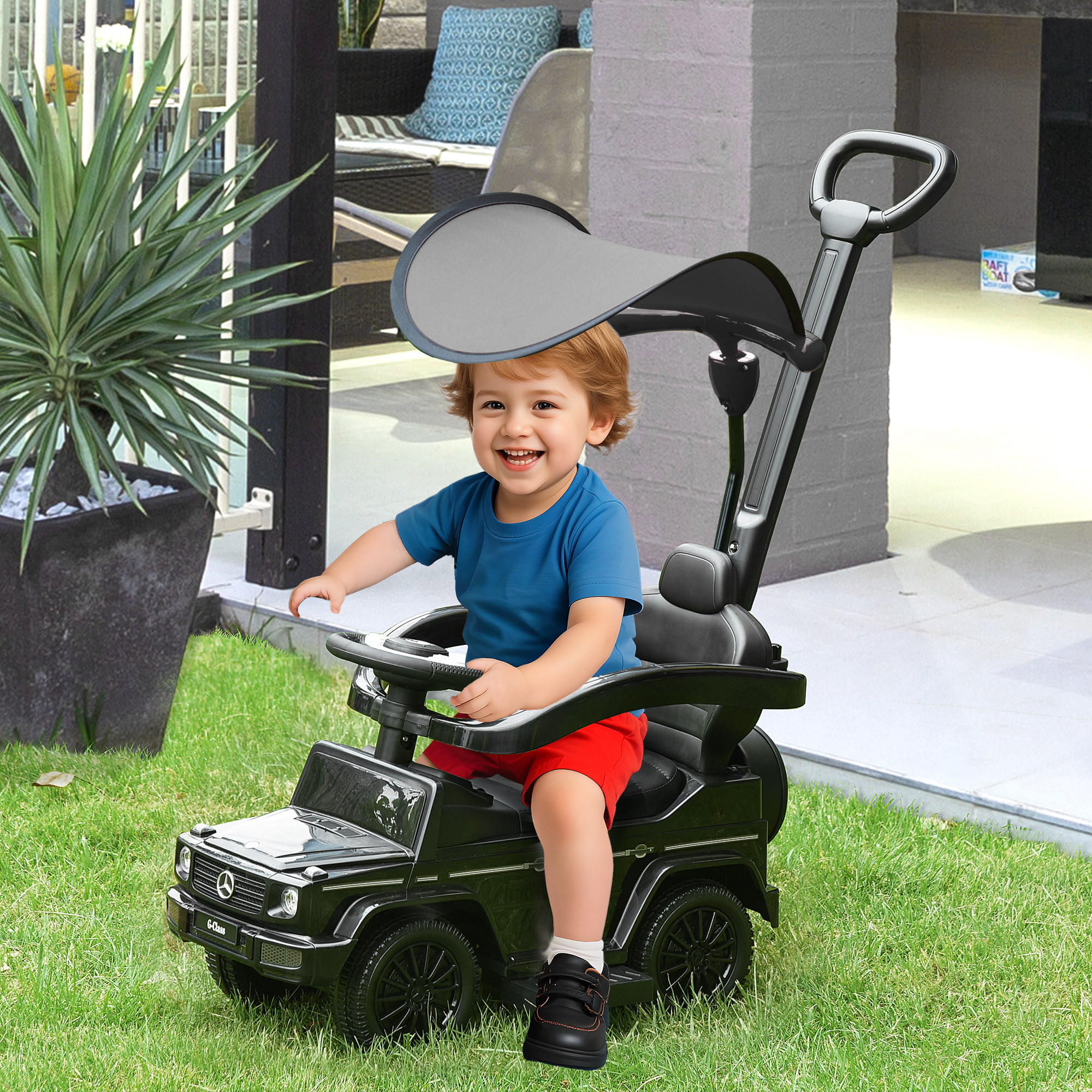 Felice bambino sorride seduto su un'auto giocattolo nera sul prato.