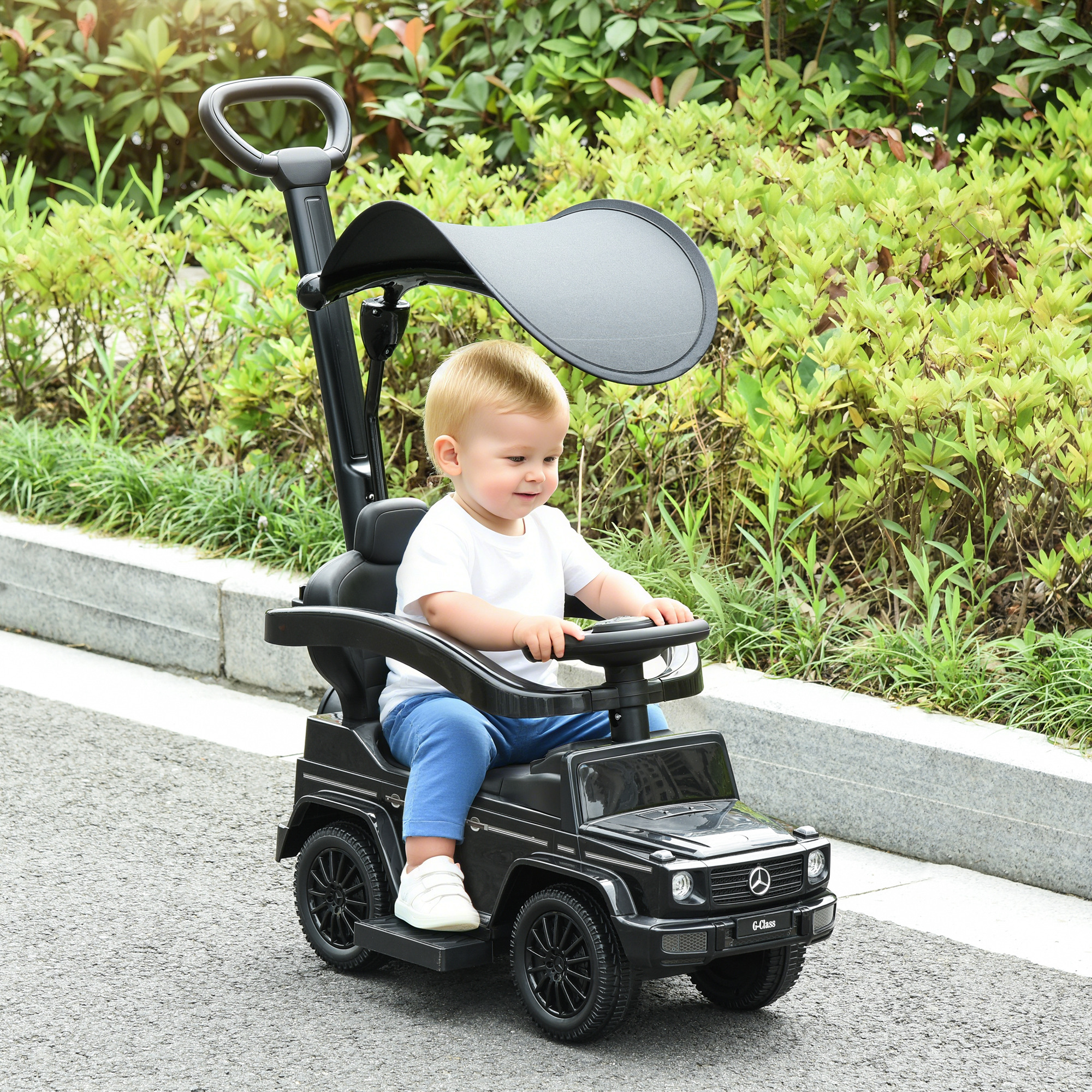 Bambino seduto su un'auto giocattolo nera con maniglione e tettuccio all'aperto.