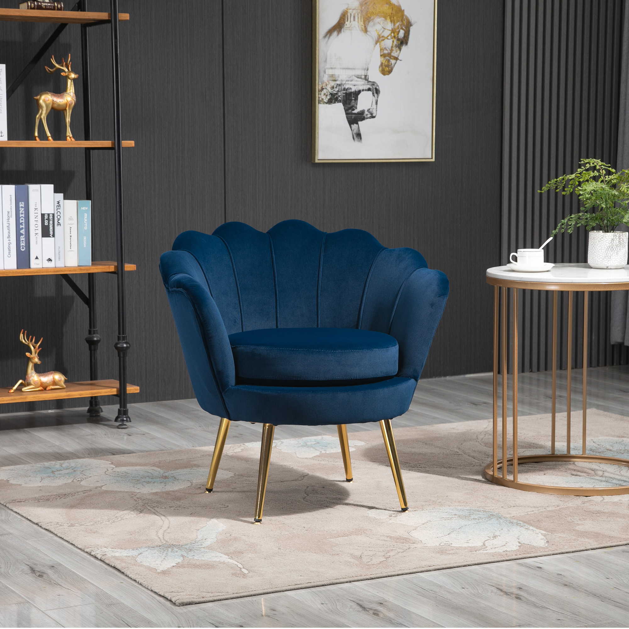Poltrona in velluto blu con gambe dorate su tappeto decorato, accanto a un tavolo e una libreria in stanza moderna.