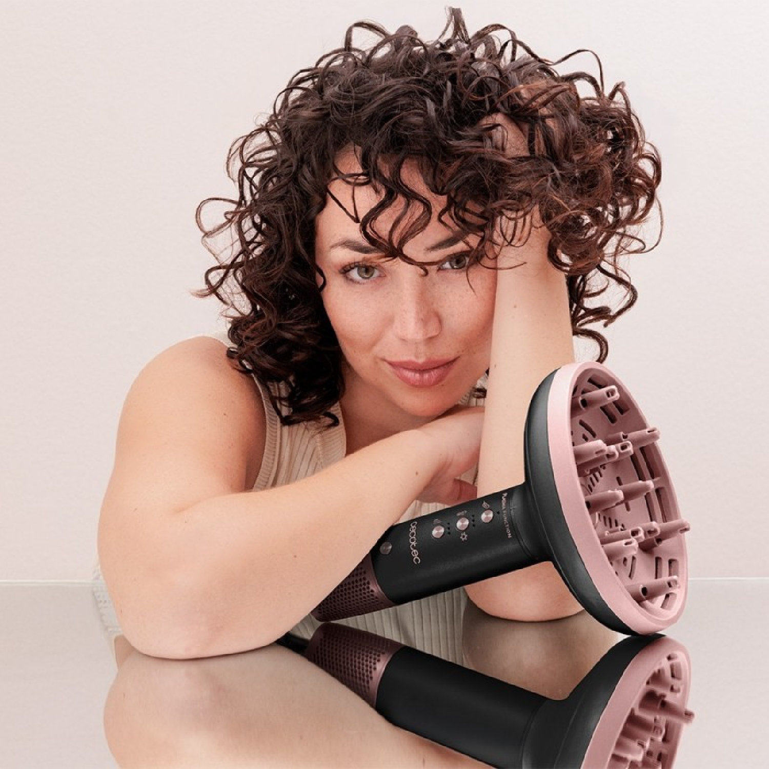 Una donna riccia poggia la testa vicino a un diffusore per capelli nero e rosa.