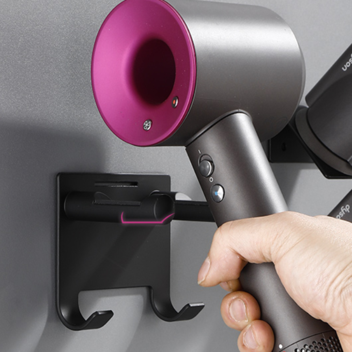 Una mano posiziona un phon grigio e magenta su un supporto da parete nero.