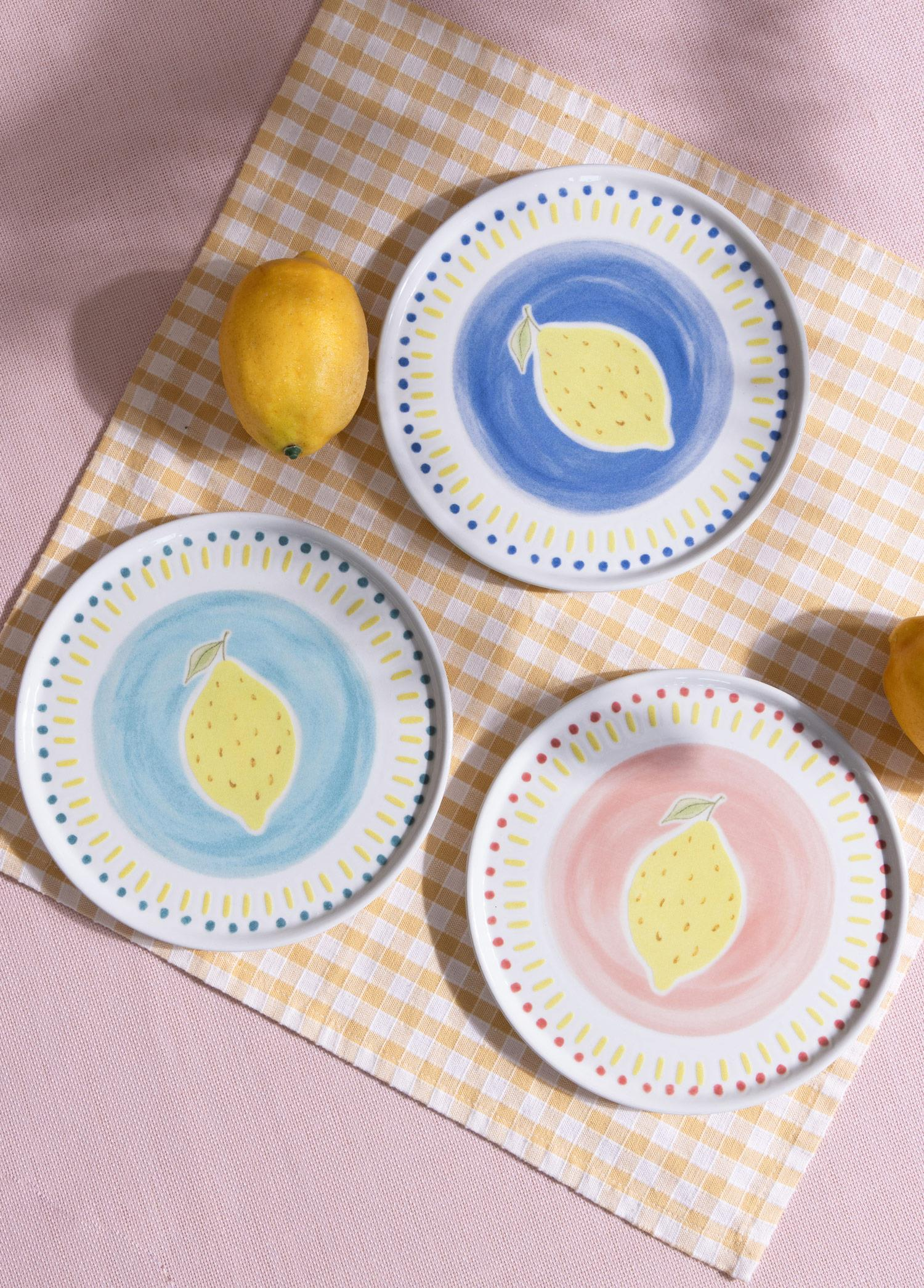 Sarı beyaz ekose bir örtü üzerinde limon desenli üç el boyaması tabak.