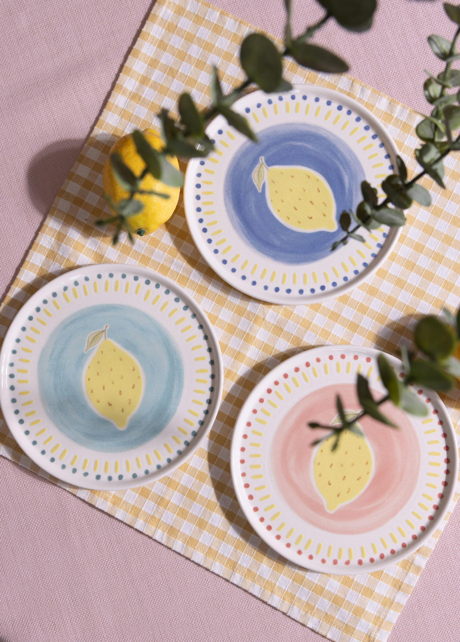 Sarı ekoseli örtü üzerinde limon desenli üç boyalı seramik tabak, gerçek bir limon ve okaliptüs dalları ile.