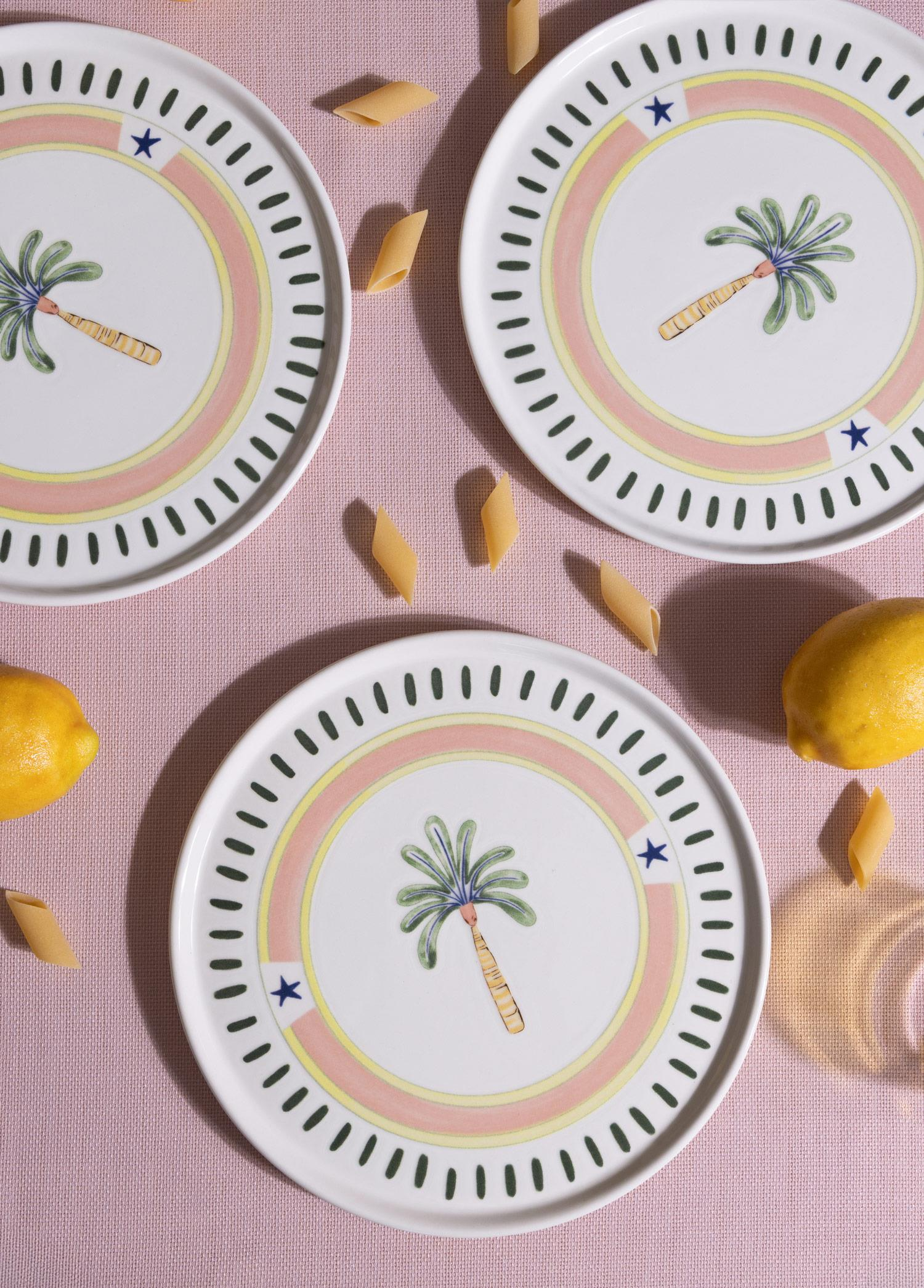 Pembe masa üzerinde palmiye desenli üç tabak, sarı limonlar ve makarna.