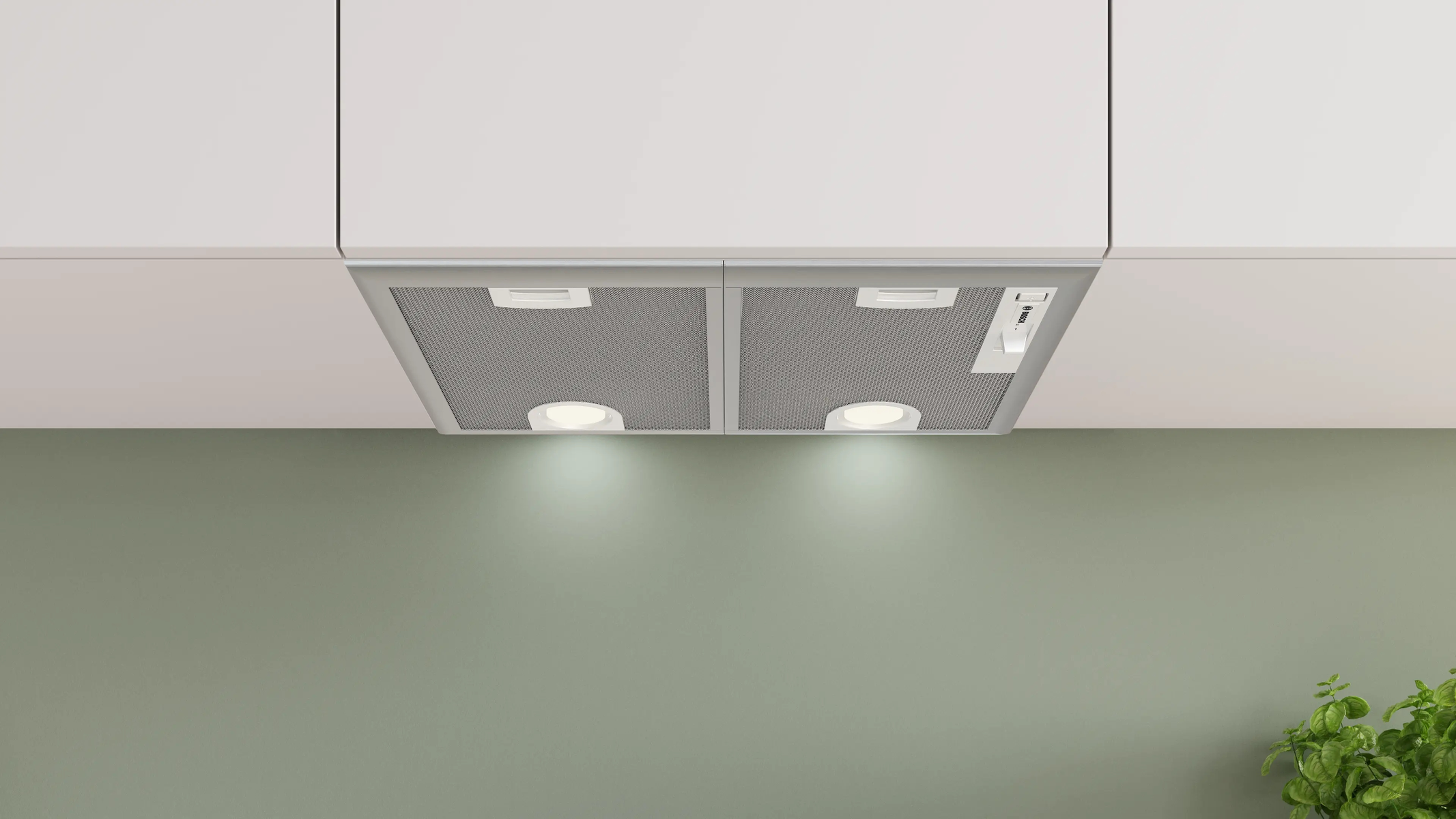 Campana extractora empotrable con luces debajo de armarios blancos contra una pared verde oliva.