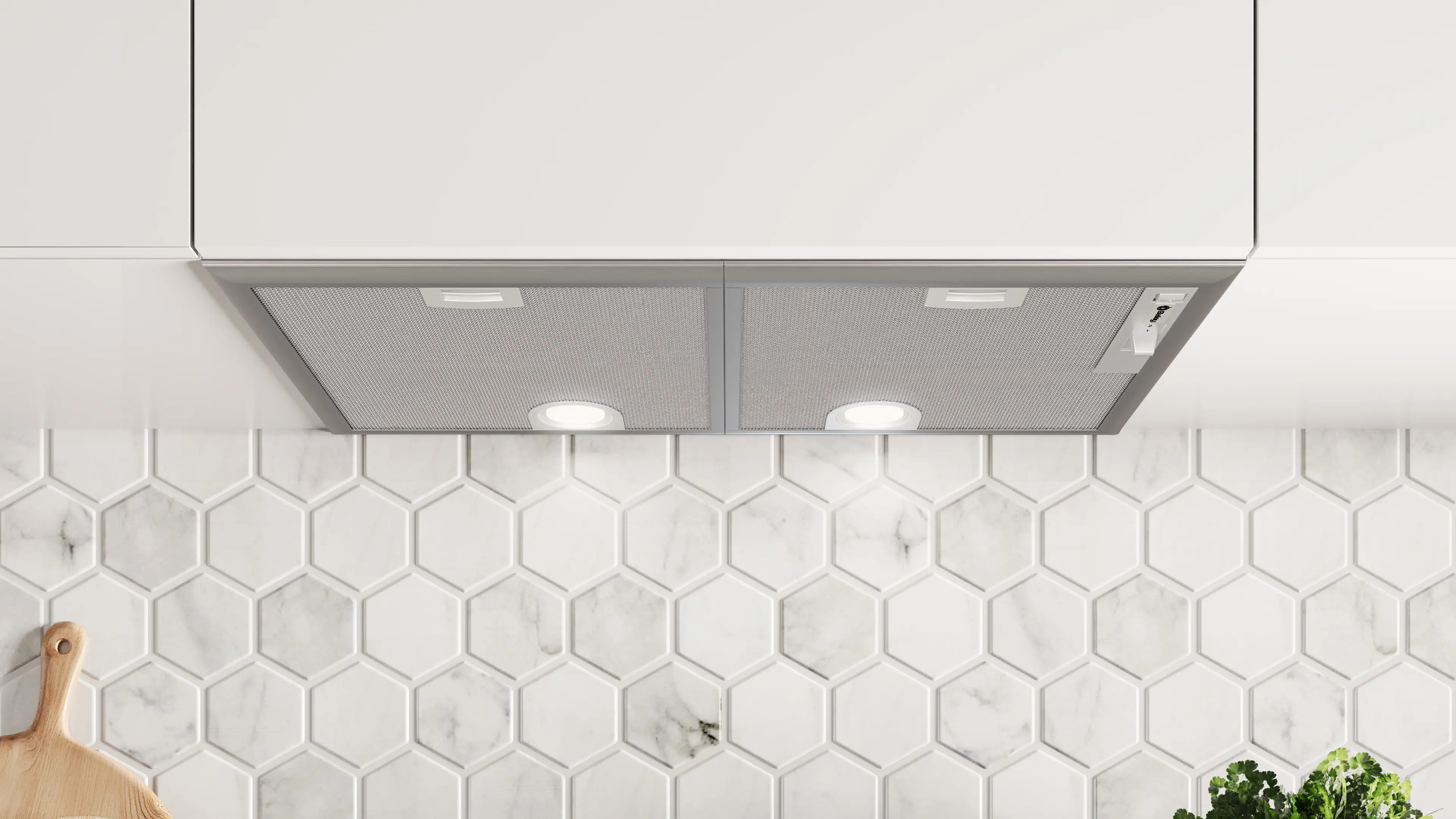 Campana extractora de acero inoxidable bajo gabinetes blancos, sobre pared de azulejos hexagonales de mármol blanco.