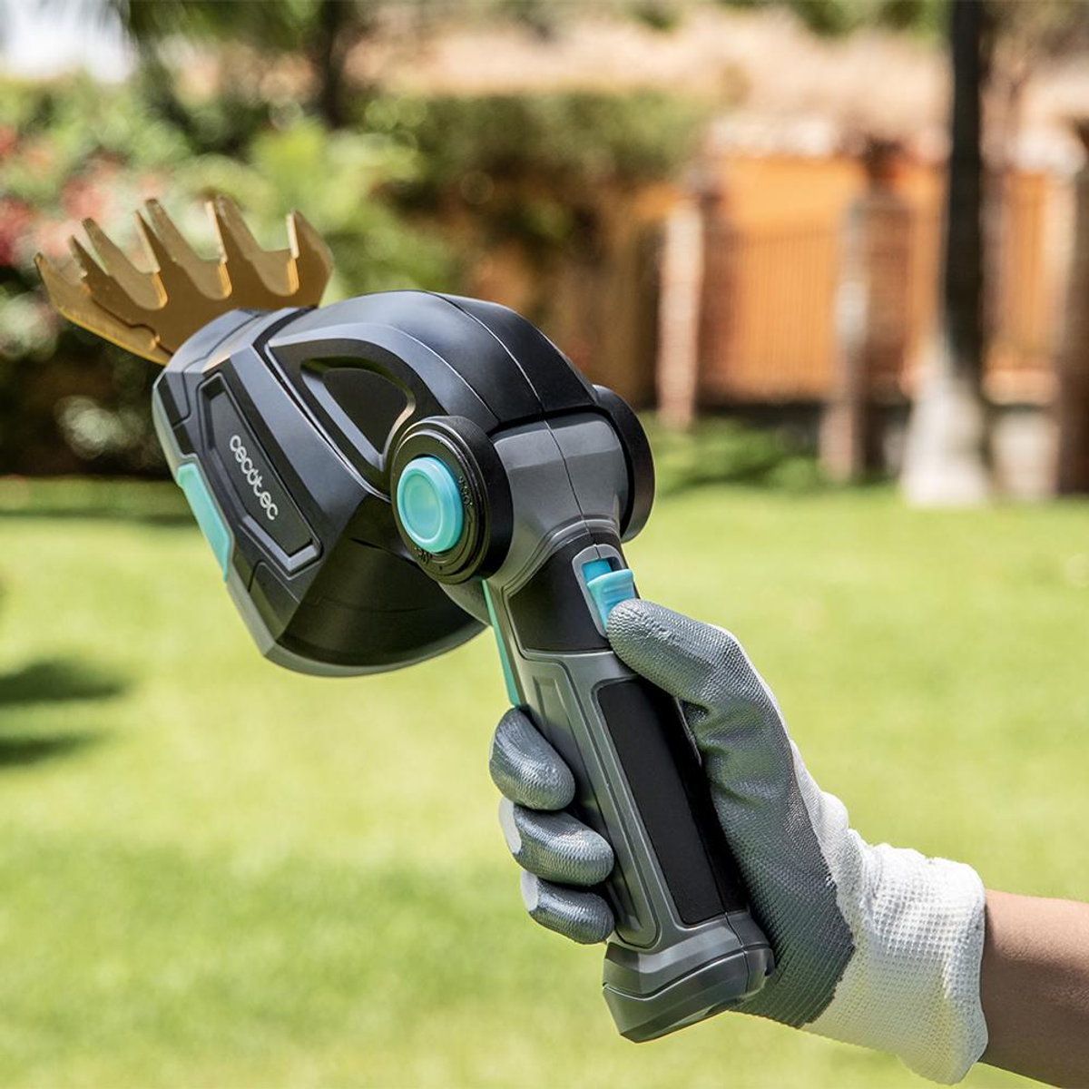 Una mano enguantada sostiene una tijera cortacésped eléctrica negra y gris en un jardín.