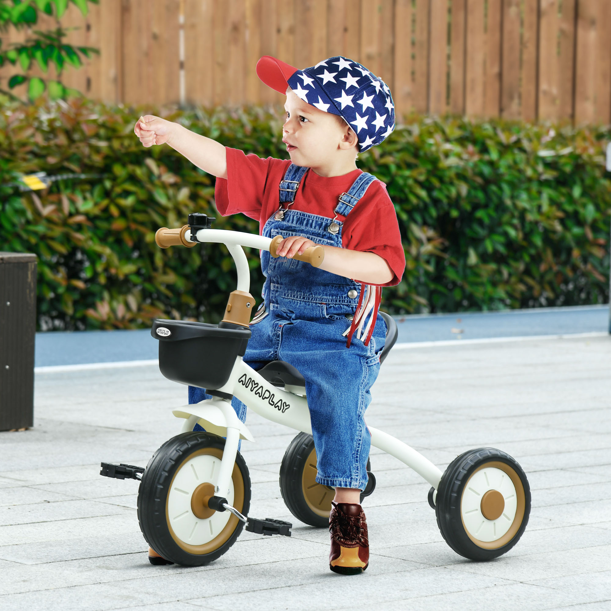 Un bambino in salopette di jeans e cappello stellato guida un triciclo indicando avanti.