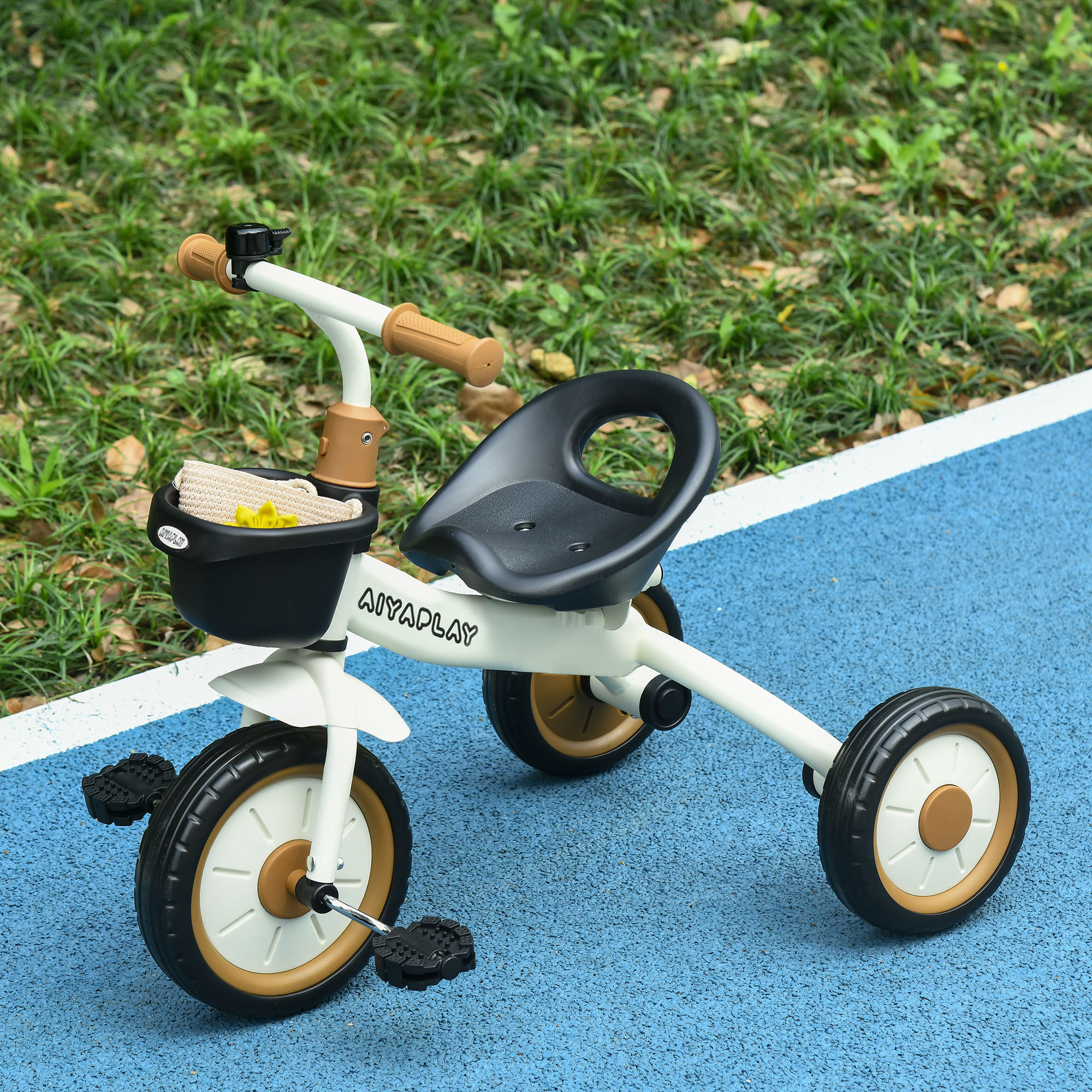 Un triciclo per bambini bianco e nero con manopole marroni e cestino anteriore su pista blu vicino all'erba.