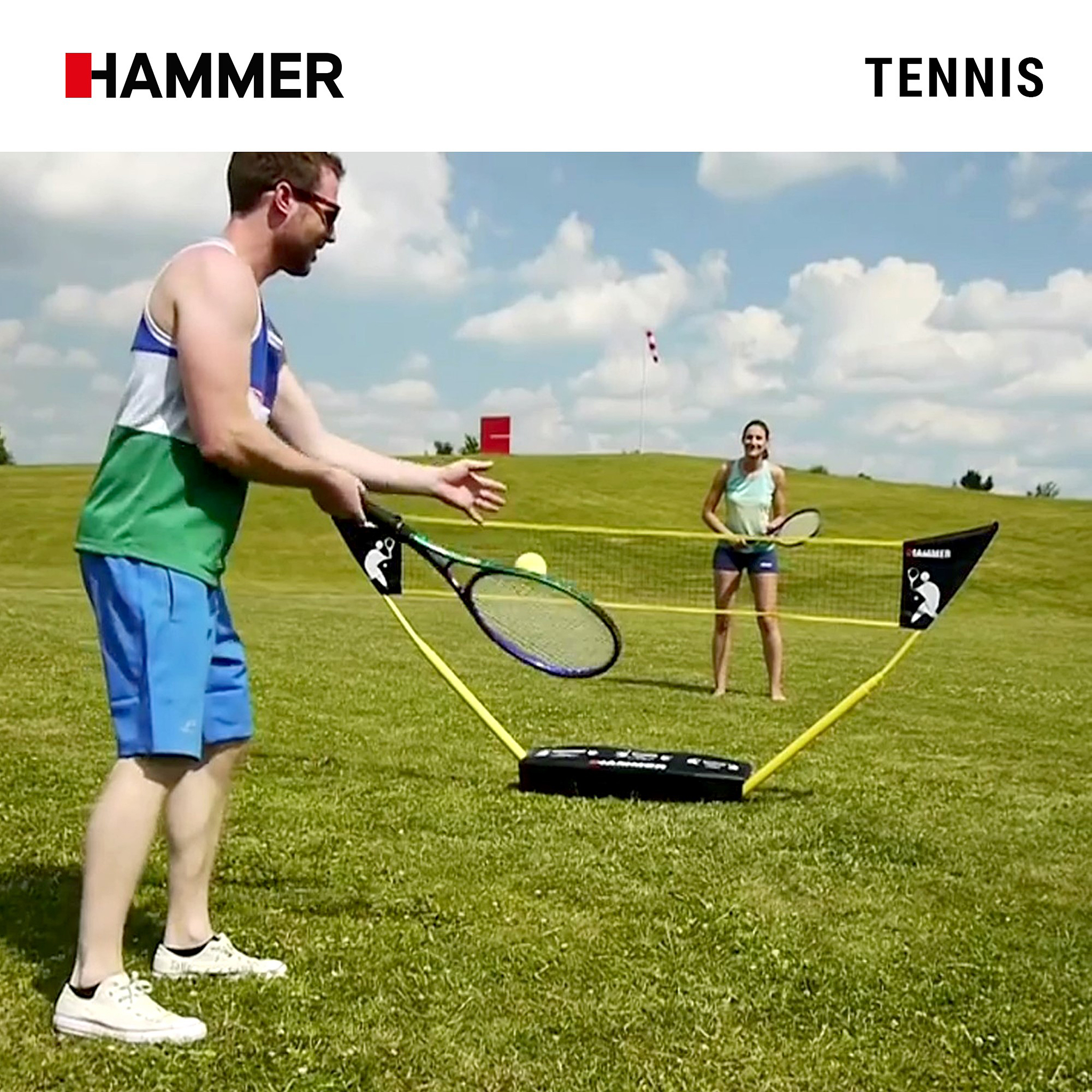 Ein Mann und eine Frau spielen Tennis im Freien auf einem Rasen mit einem tragbaren Netz unter einem bewölkten Himmel.