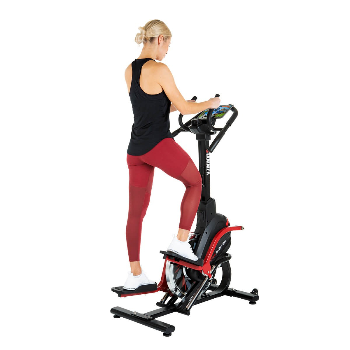 Eine blonde Frau in schwarzem Tanktop und roten Leggings trainiert auf einem schwarzen und roten Heimtrainer.