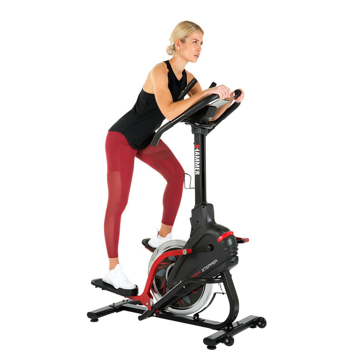 Eine blonde Frau in schwarzem Oberteil und roten Leggings trainiert auf einem schwarz-roten Hammer Cross Stepper vor weißem Hintergrund.