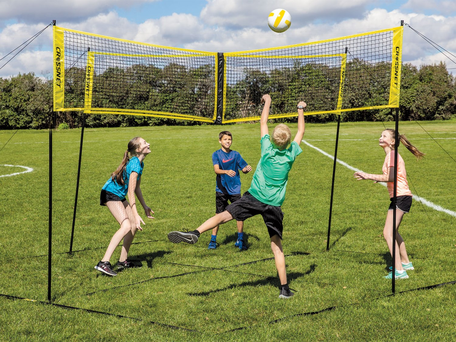 Vier Kinder spielen Vier-Wege-Volleyball auf einem Rasenplatz im Freien.