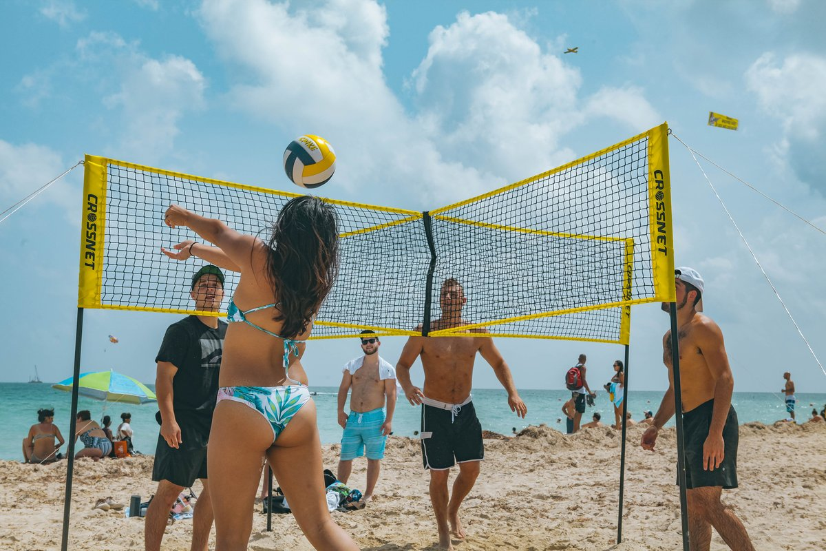 Freunde spielen Volleyball an einem sonnigen Strand mit blauem Himmel.