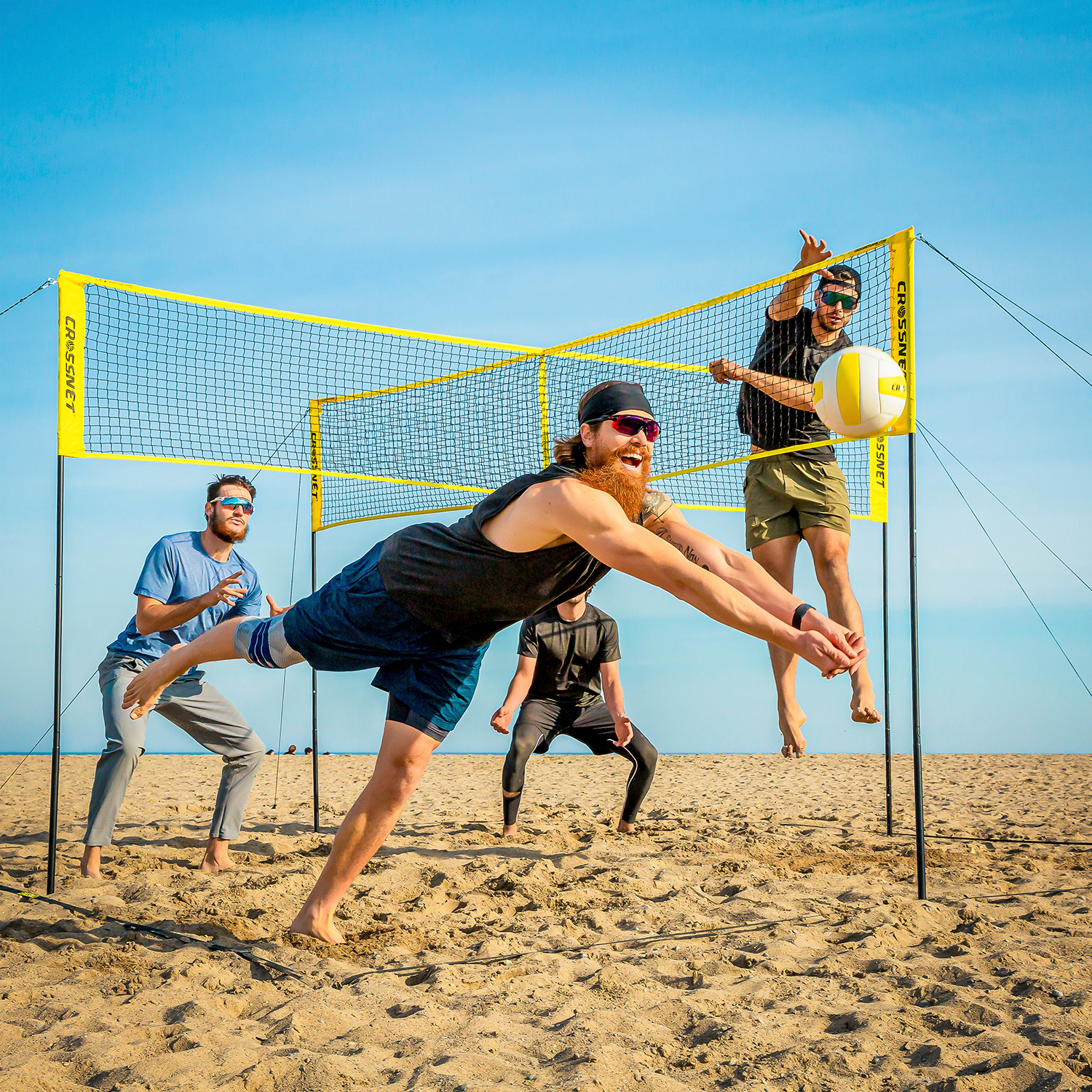 Vier Männer spielen Beachvolleyball auf sandigem Boden an einem sonnigen Tag.