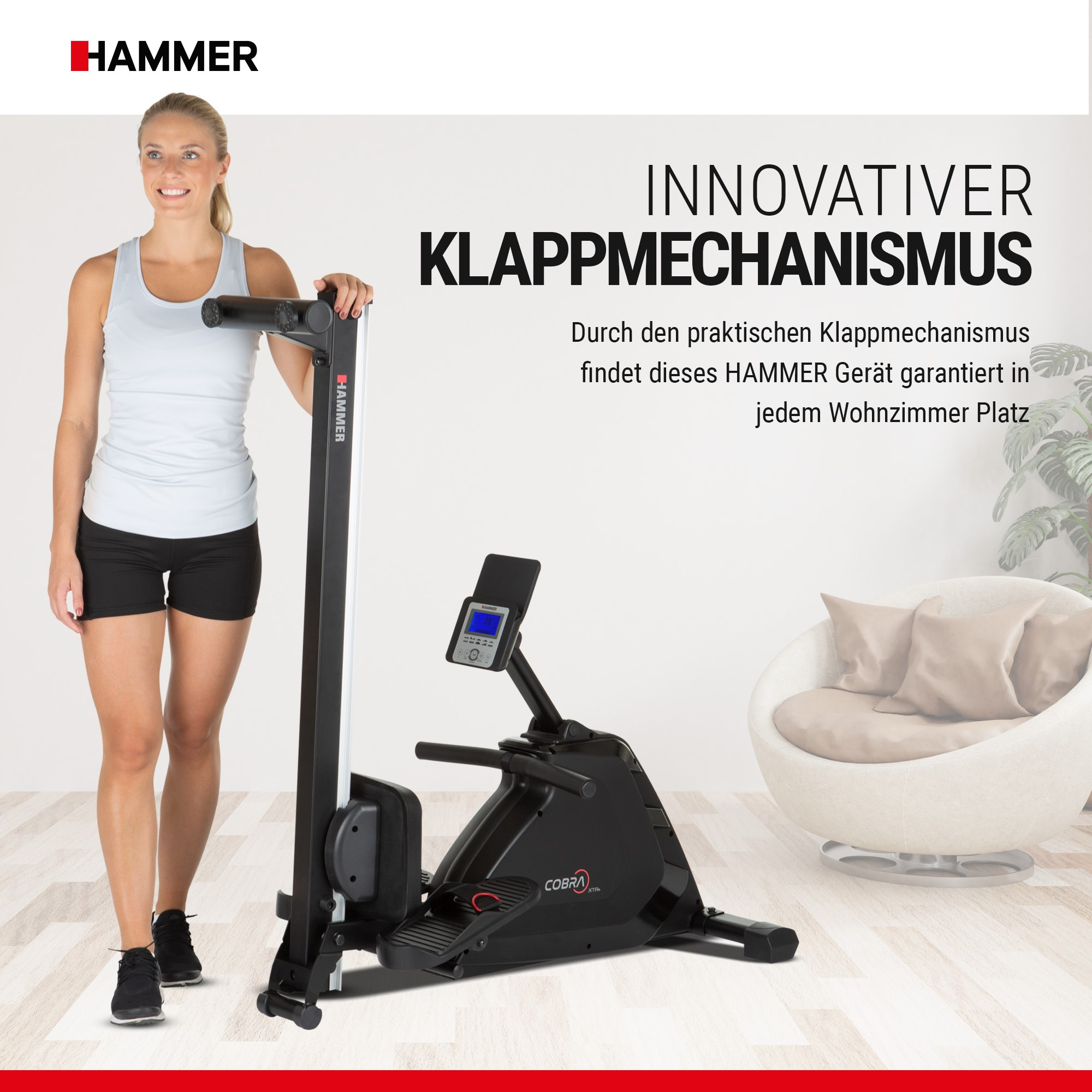 Eine Frau steht neben einem zusammengeklappten schwarzen Rudergerät in einem hellen Zimmer mit weißem Sessel.