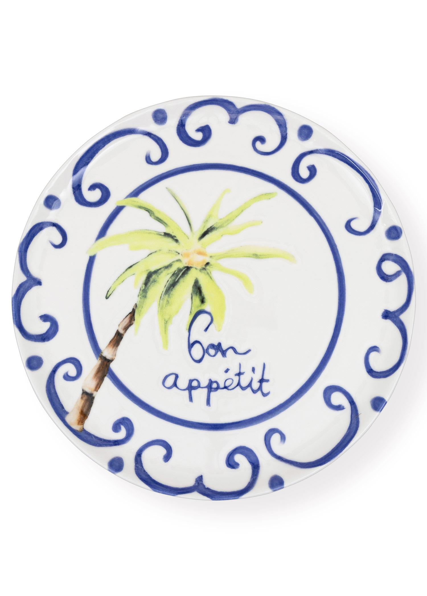 Ortasında mavi girdap deseni, sarı palmiye ağacı ve "Bon appétit" yazısı bulunan beyaz bir tabak.