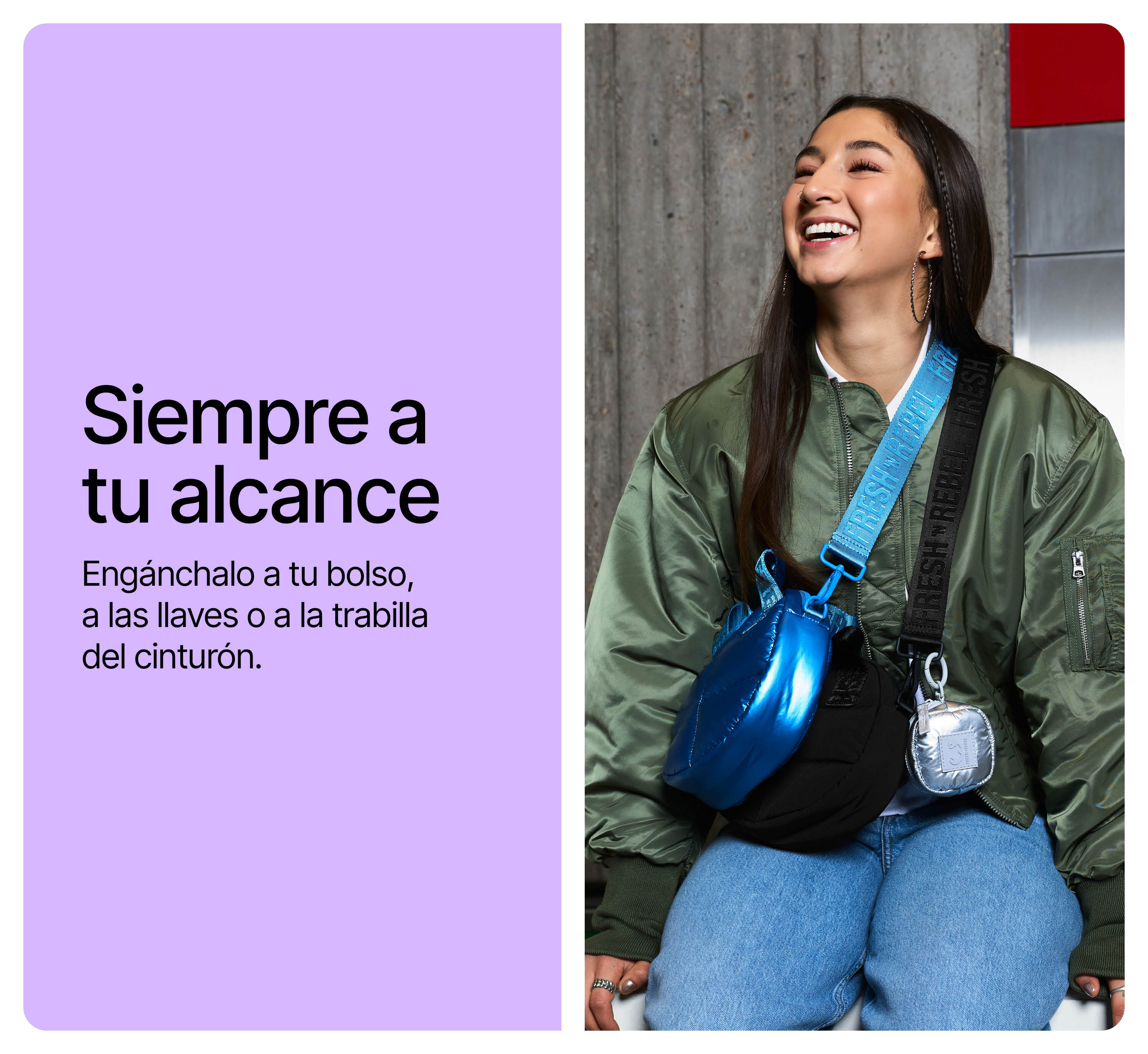 Una mujer sonriente con chaqueta verde lleva bolsos azules y negros con correas coloridas ante un muro gris.
