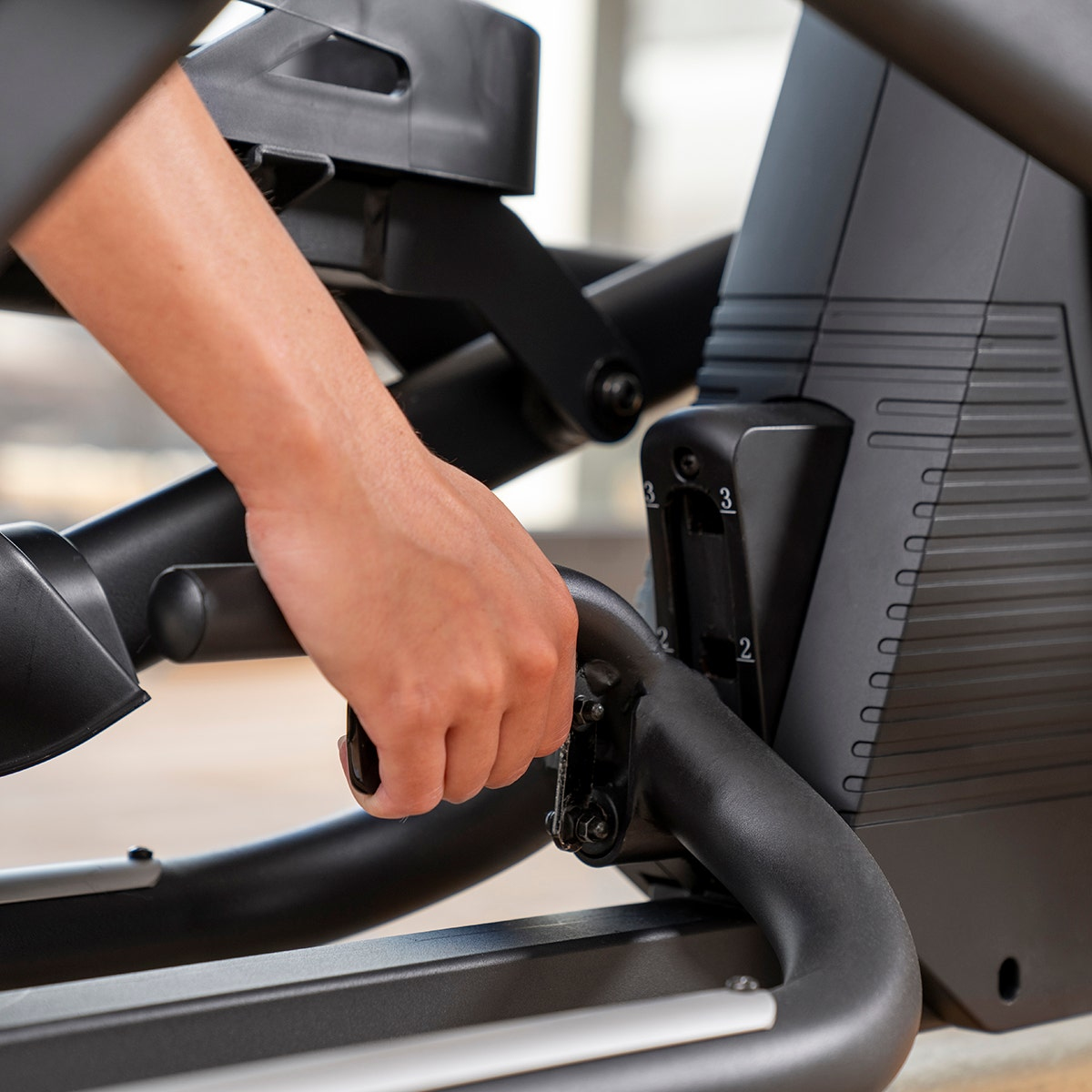 Eine Hand greift nach dem Griff einer schwarzen Crosstrainer-Maschine in einem Fitnessstudio.