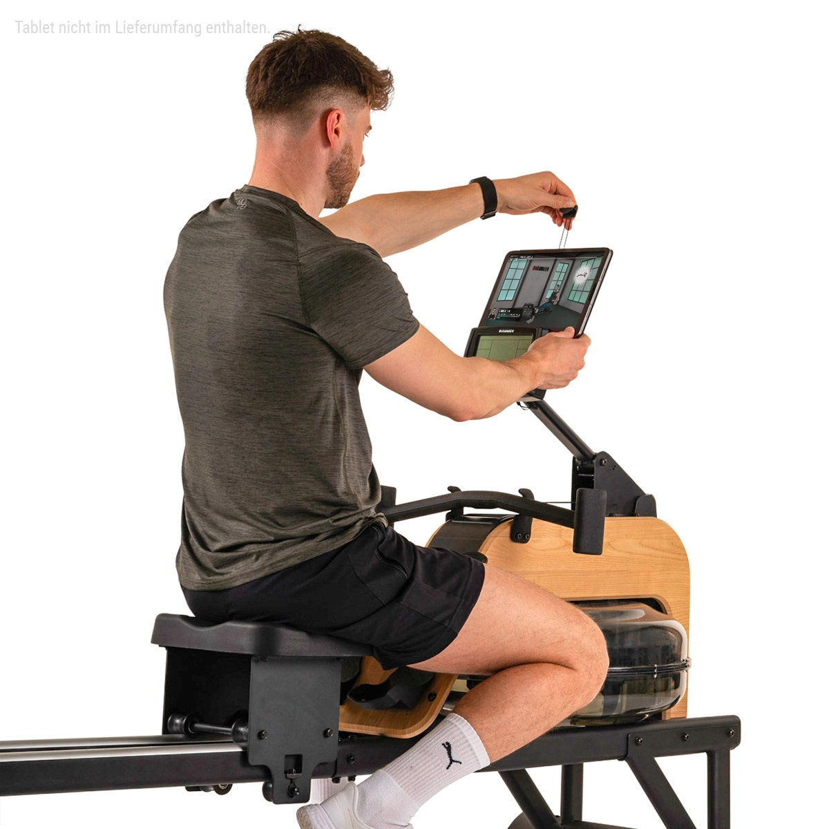 Ein Mann in grünem Shirt und schwarzen Shorts nutzt ein Holz-Wasser-Rudergerät und bedient ein Tablet.