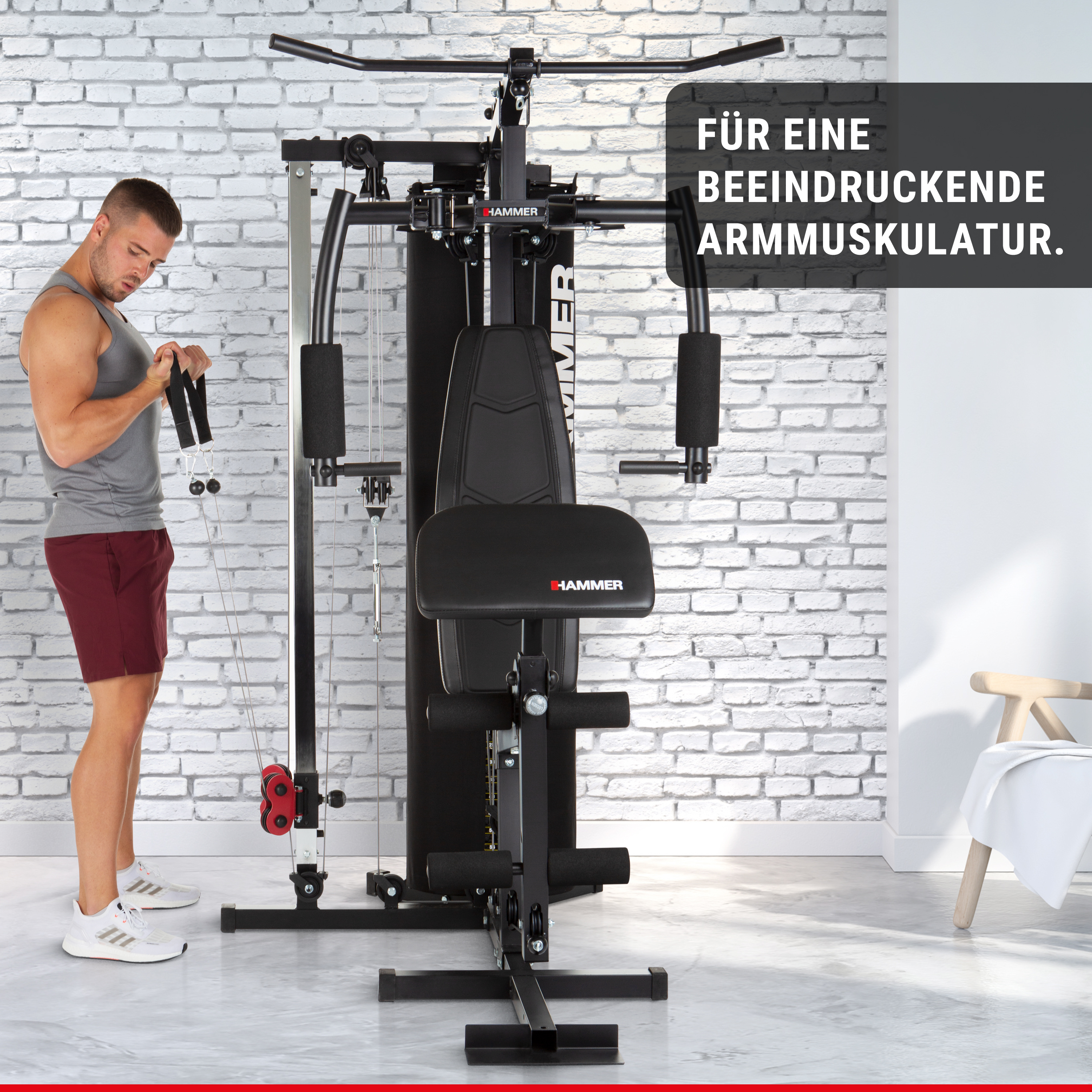 Ein Mann im grauen Tanktop trainiert an einer schwarzen Kraftstation vor einer weißen Ziegelwand.