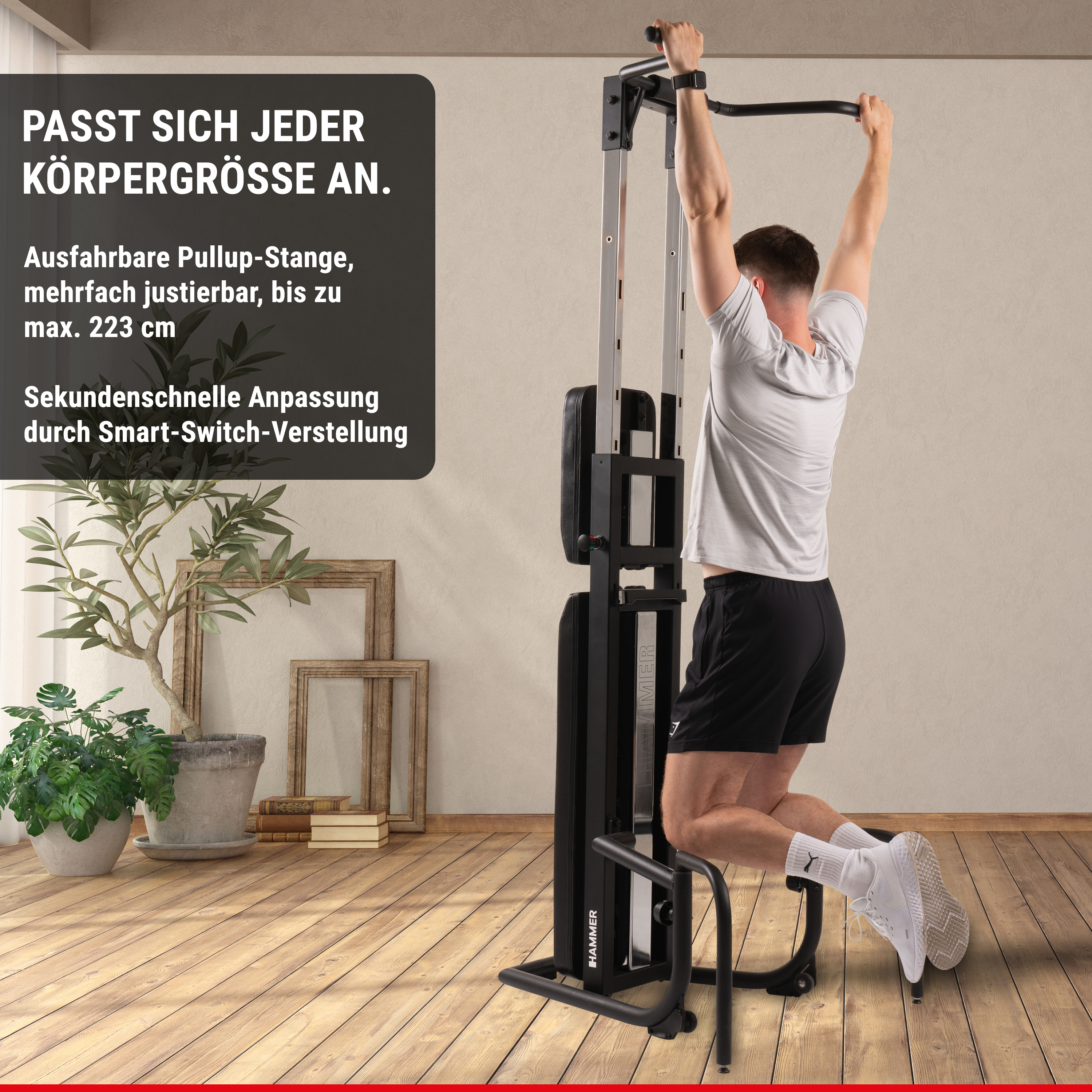 Ein Mann übt an einer schwarzen Klimmzugstation in einem Raum mit Pflanzen und Holzrahmen im Hintergrund.