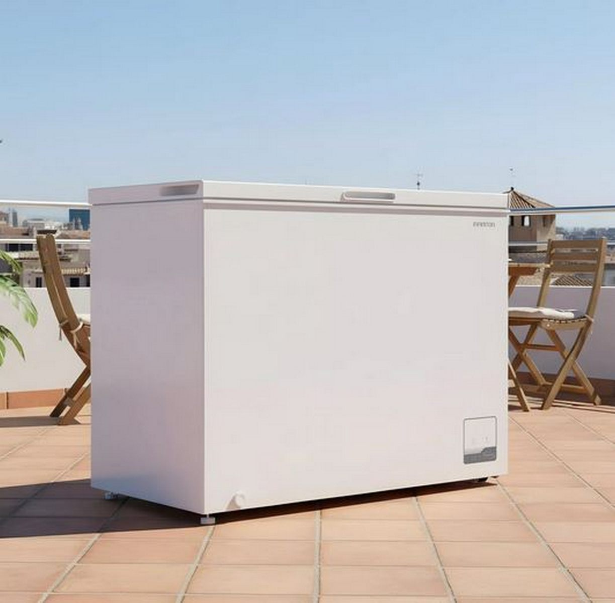 Un congelador horizontal blanco en una soleada terraza en la azotea con suelo de baldosas y sillas de madera.