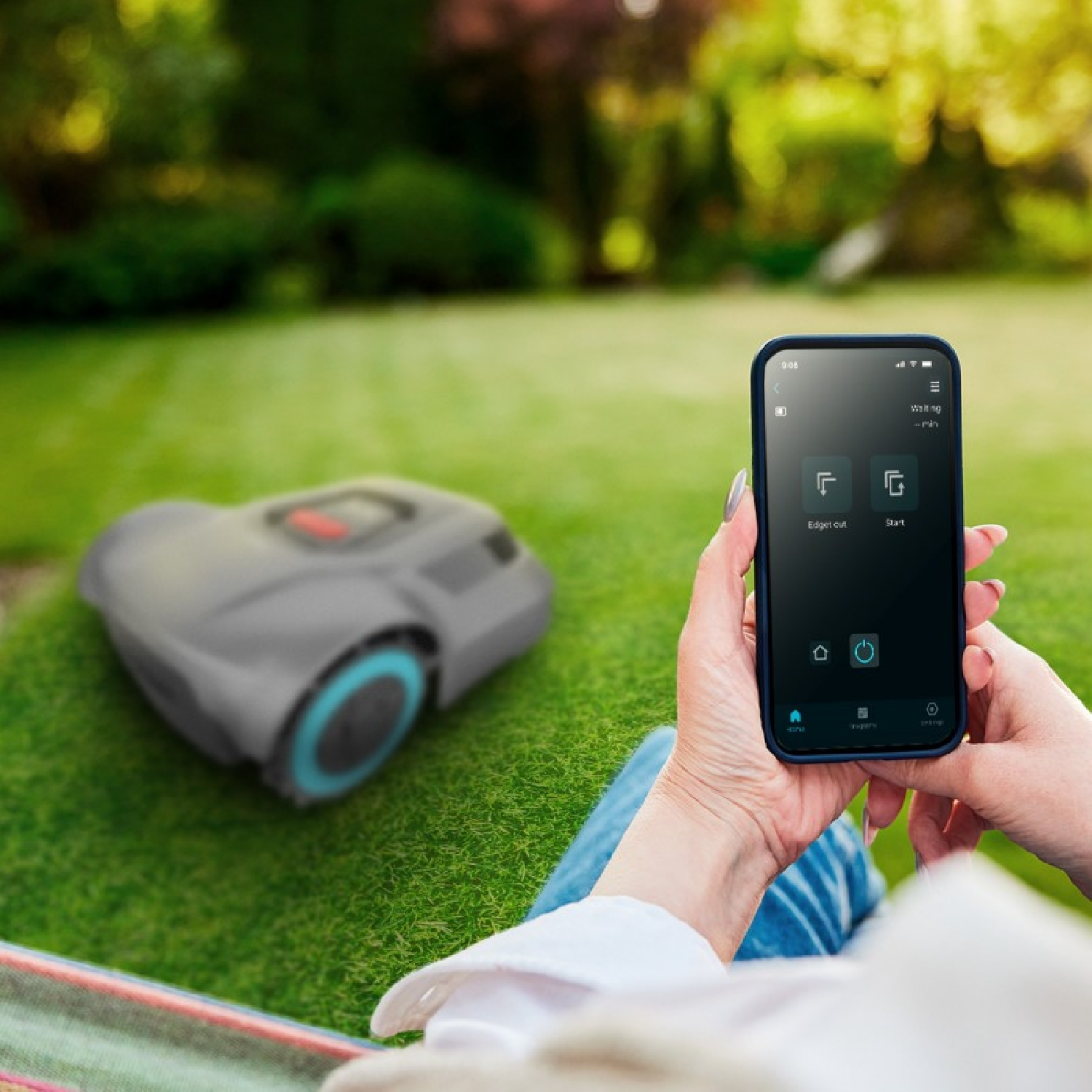 Una persona sostiene un teléfono con una app de cortacésped robótico, con un robot cortacésped de fondo en el césped.