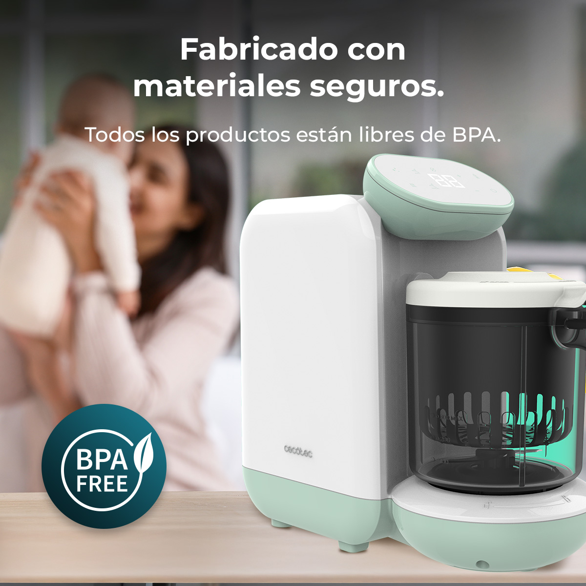 Un cuocipappa bianco e verde su un tavolo, con una madre che tiene in braccio il suo bambino sullo sfondo. Senza BPA.