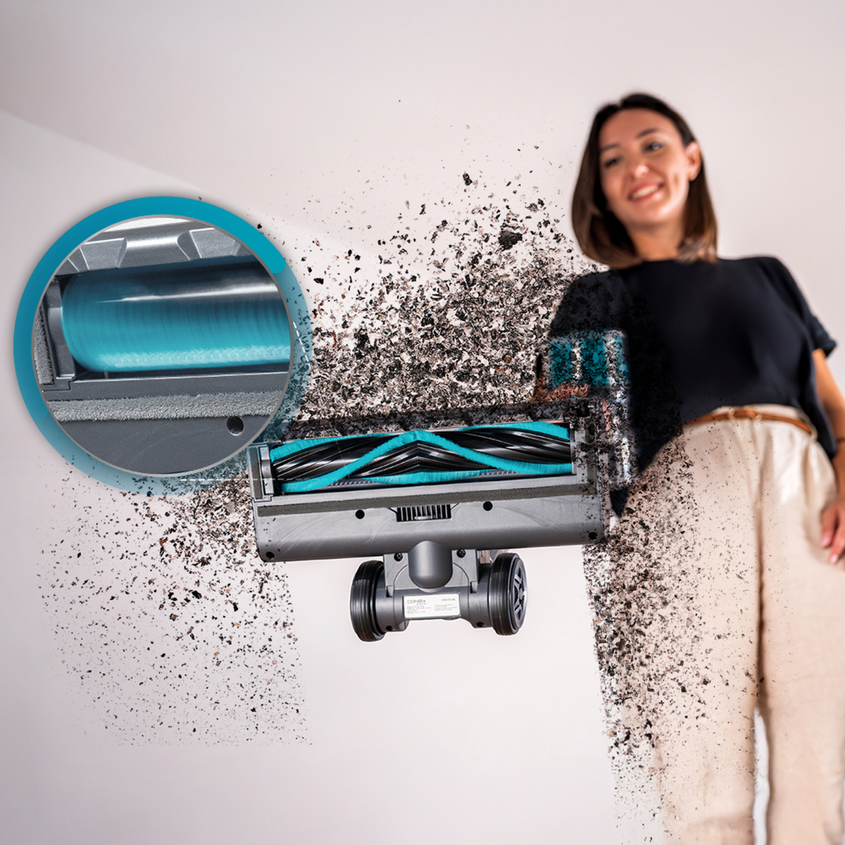 A woman holds a vacuum brush, surrounded by flying debris and a circular inset showing the roller mechanism.
