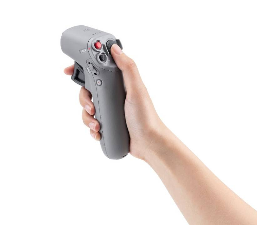 Eine Hand hält einen grauen Drohnencontroller mit Tasten und Joystick vor weißem Hintergrund.