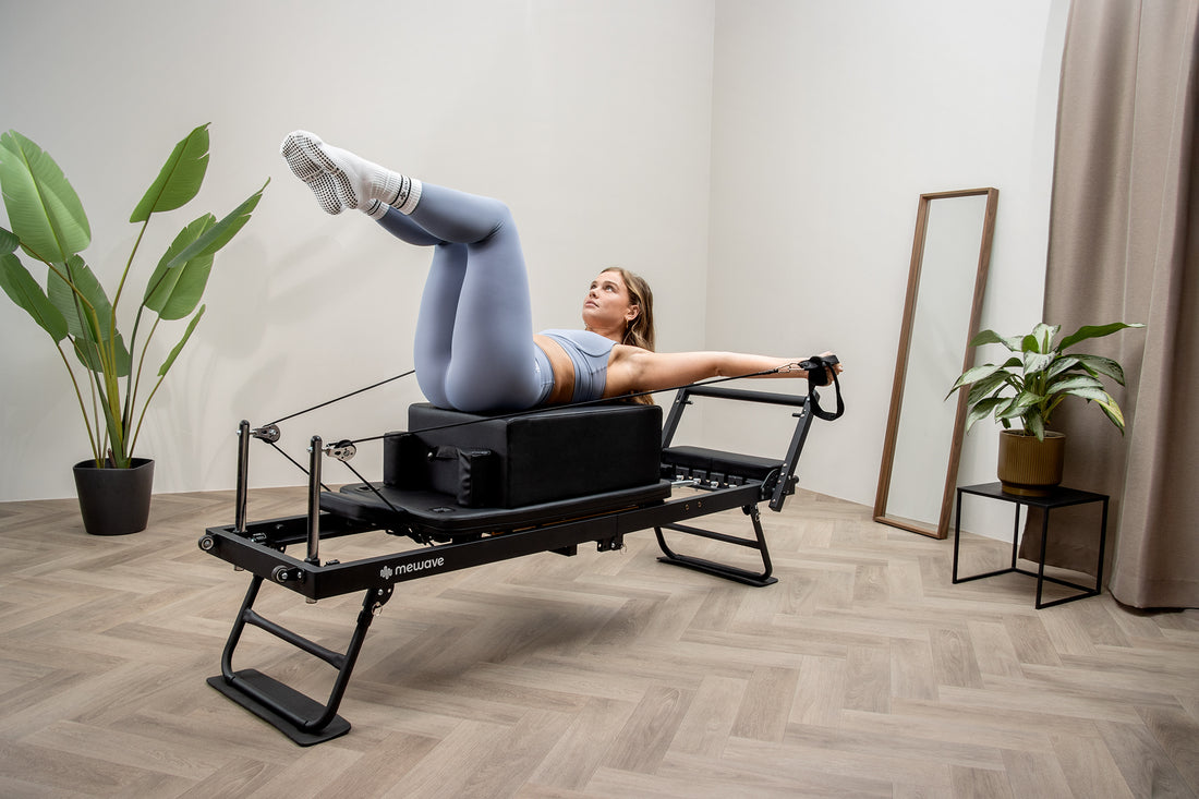 Una donna in abbigliamento sportivo blu fa Pilates su una macchina reformer in una stanza luminosa.