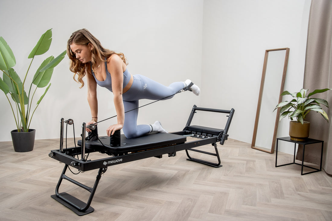 Una donna in abbigliamento sportivo blu usa una macchina per pilates nera in interni, con piante e specchio.