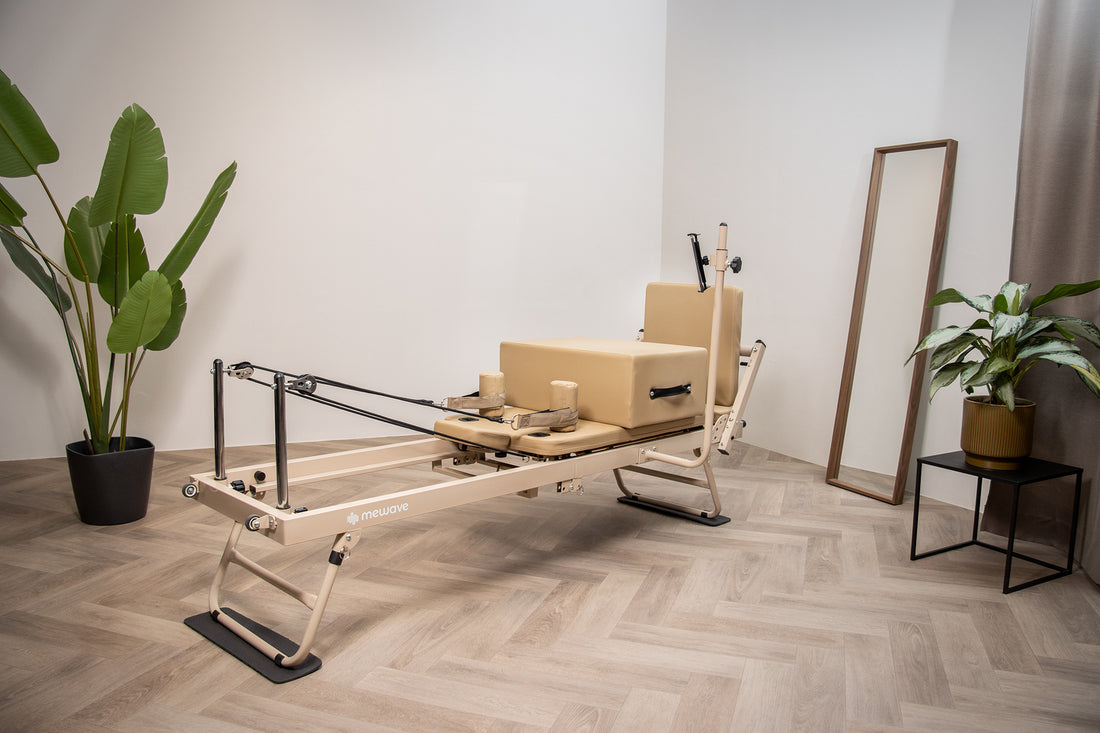 Un reformer per pilates beige in una stanza luminosa con pavimento in legno, piante e specchio.