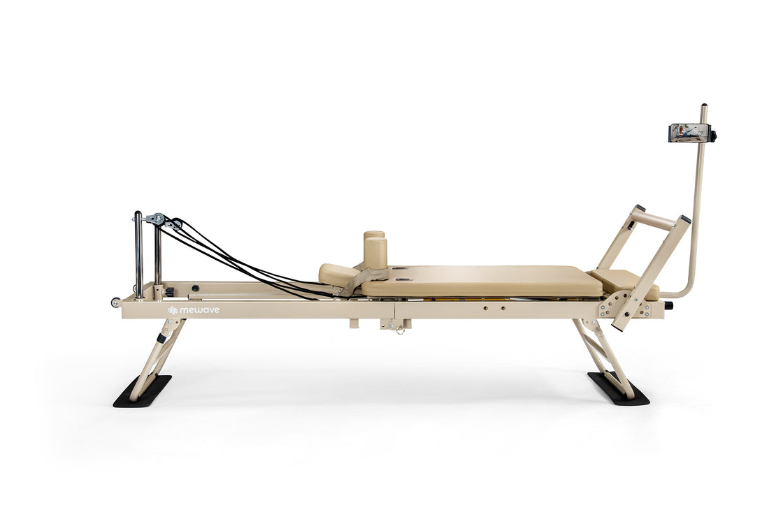 Macchina reformer per pilates beige con cinghie nere e supporto per smartphone su sfondo bianco.