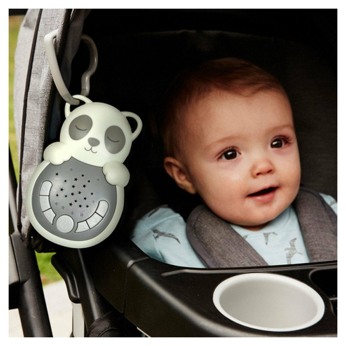 Ein Baby sitzt in einem Kinderwagen, während ein panda-förmiges Soundgerät in der Nähe hängt.