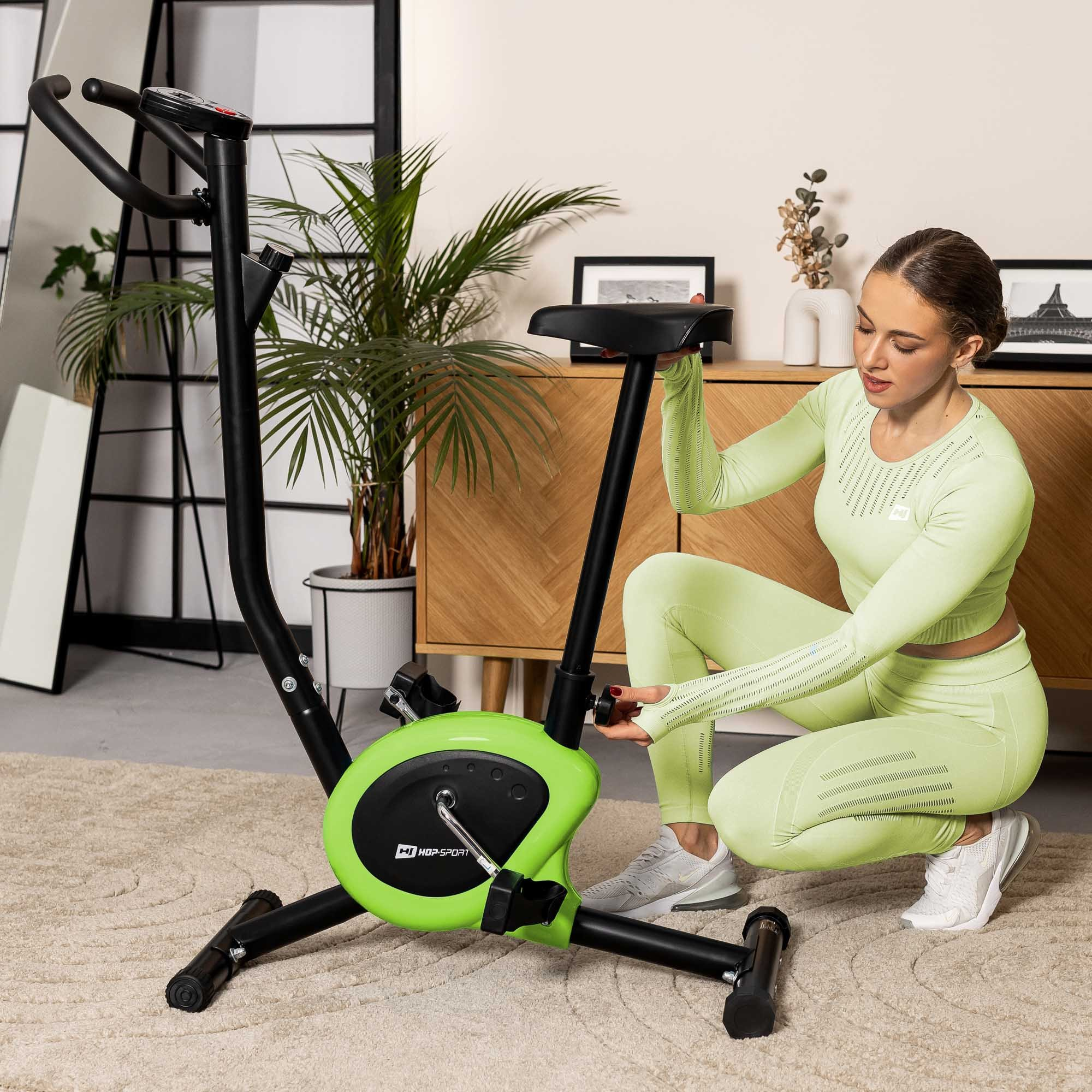 Eine Frau in hellgrüner Sportkleidung adjusting the height of a stationary exercise bike.