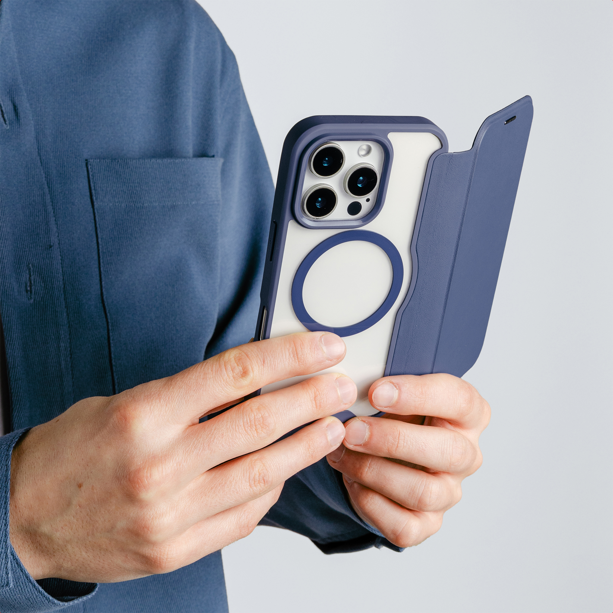 Eine Person in einem blauen Hemd hält ein Smartphone mit blauer Schutzhülle vor hellem Hintergrund.