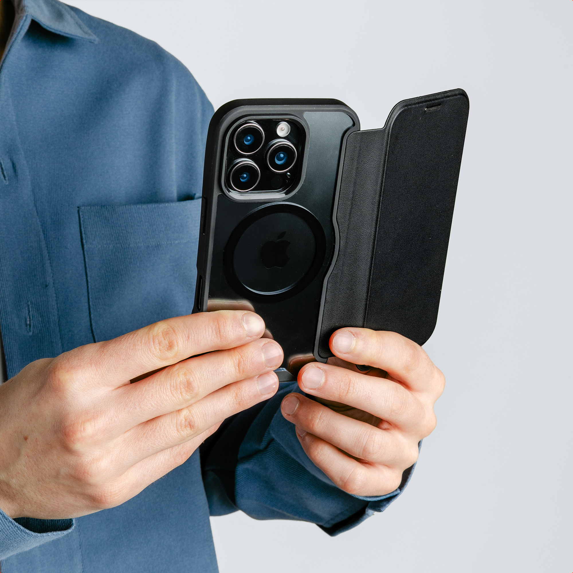 Eine Person in einem blauen Hemd hält ein Smartphone mit schwarzer Hülle und offener Klappe.